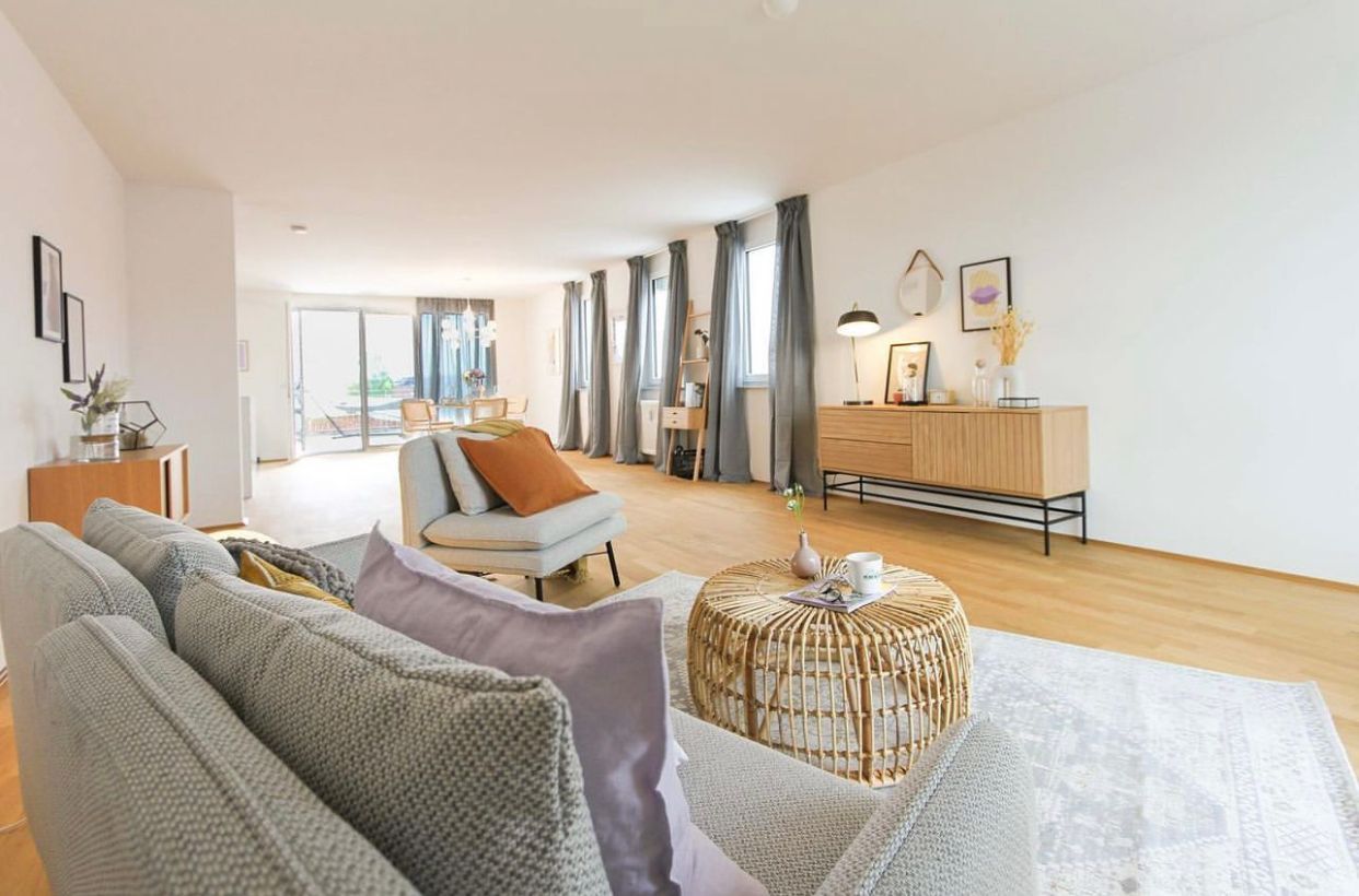 Bright modern living room with gray sofa, orange chair, woven poufs, and large windows