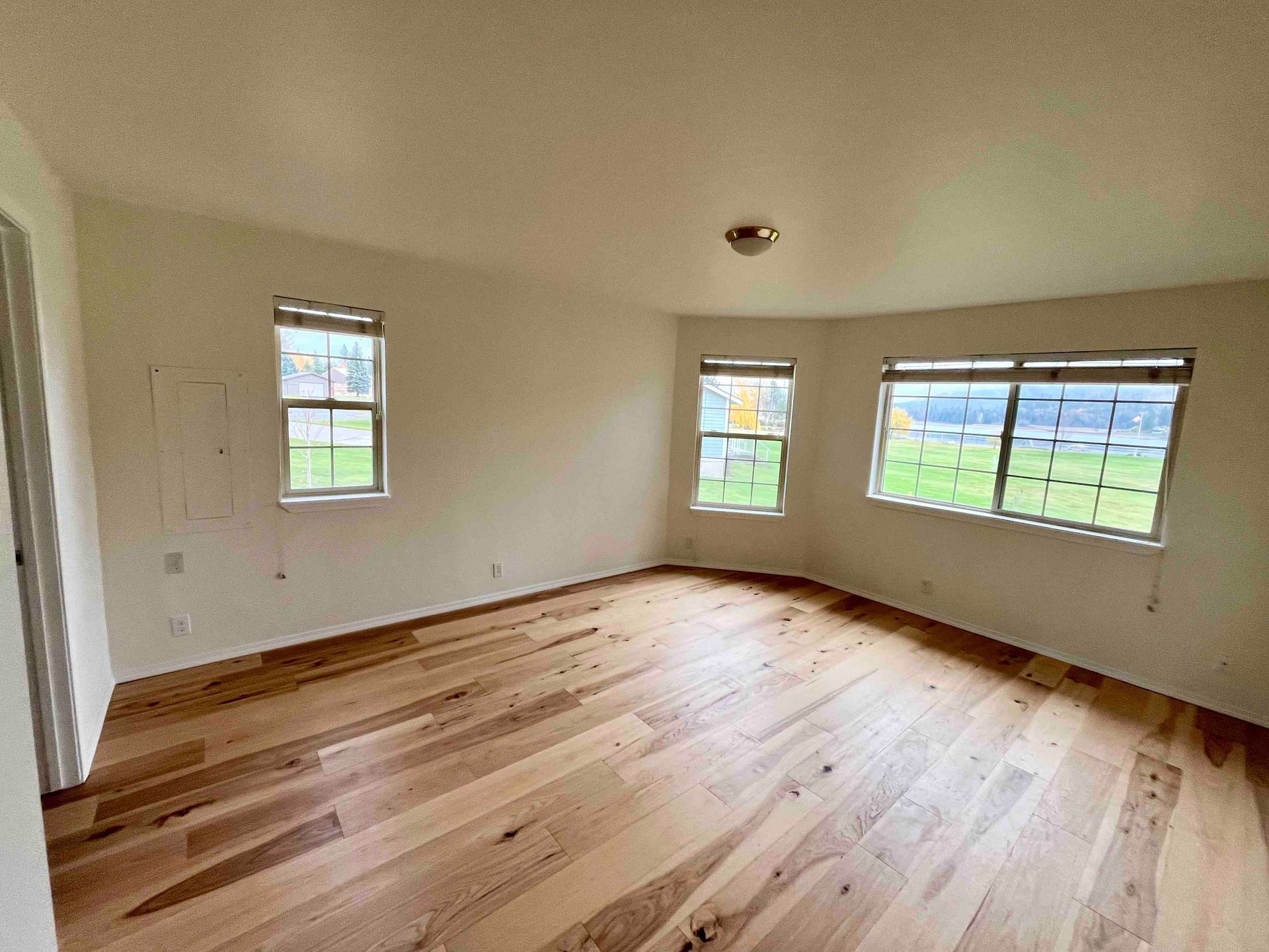 Empty unfurnished room with hardwood floors, white walls, and large windows overlooking a green view