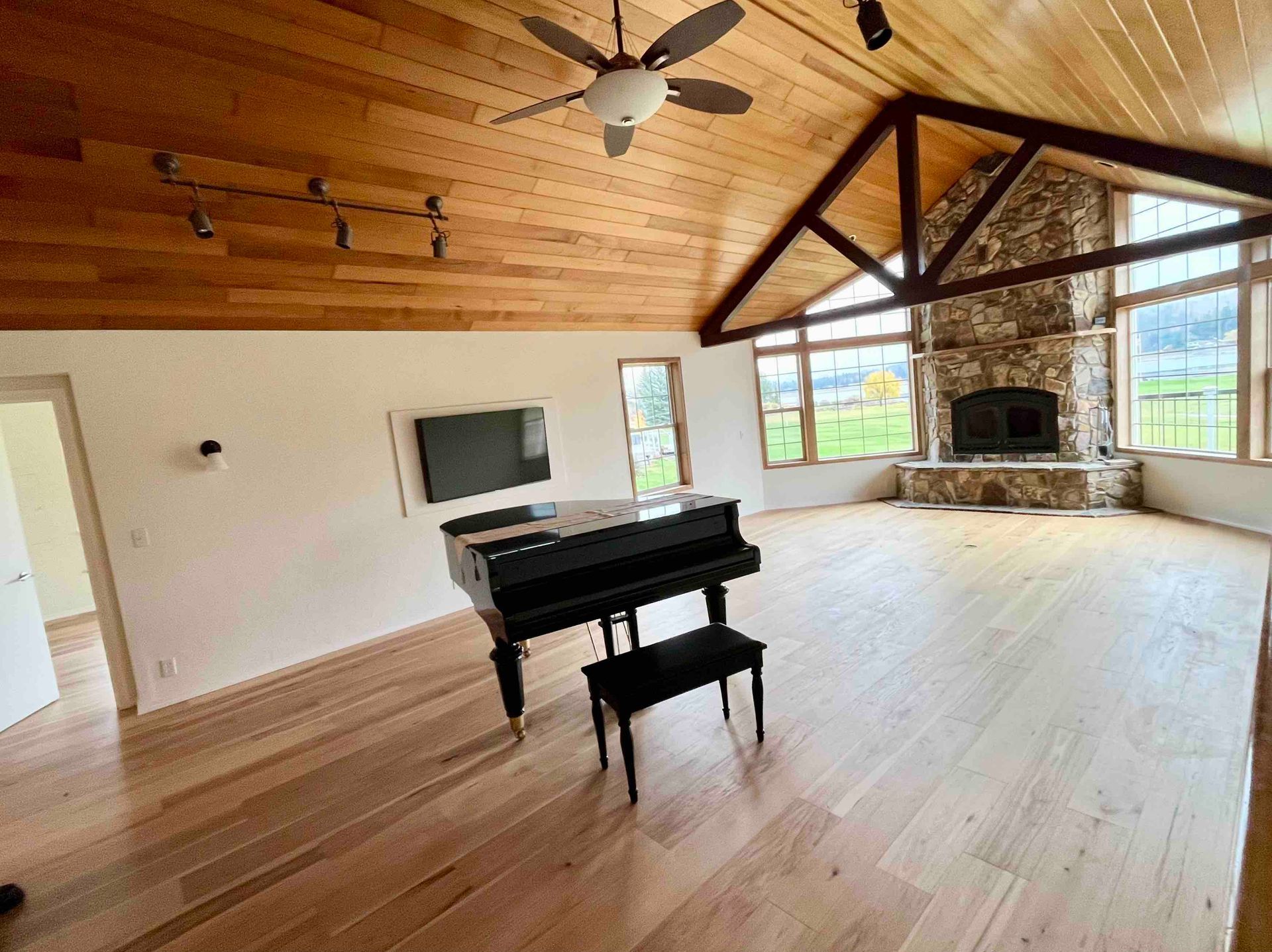 Spacious living room with a grand piano, vaulted wood ceiling, fireplace, and large windows