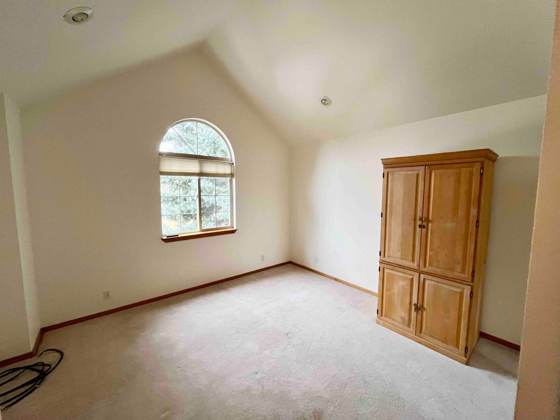 Empty beige bedroom with a arched window and a wooden wardrobe against the wall