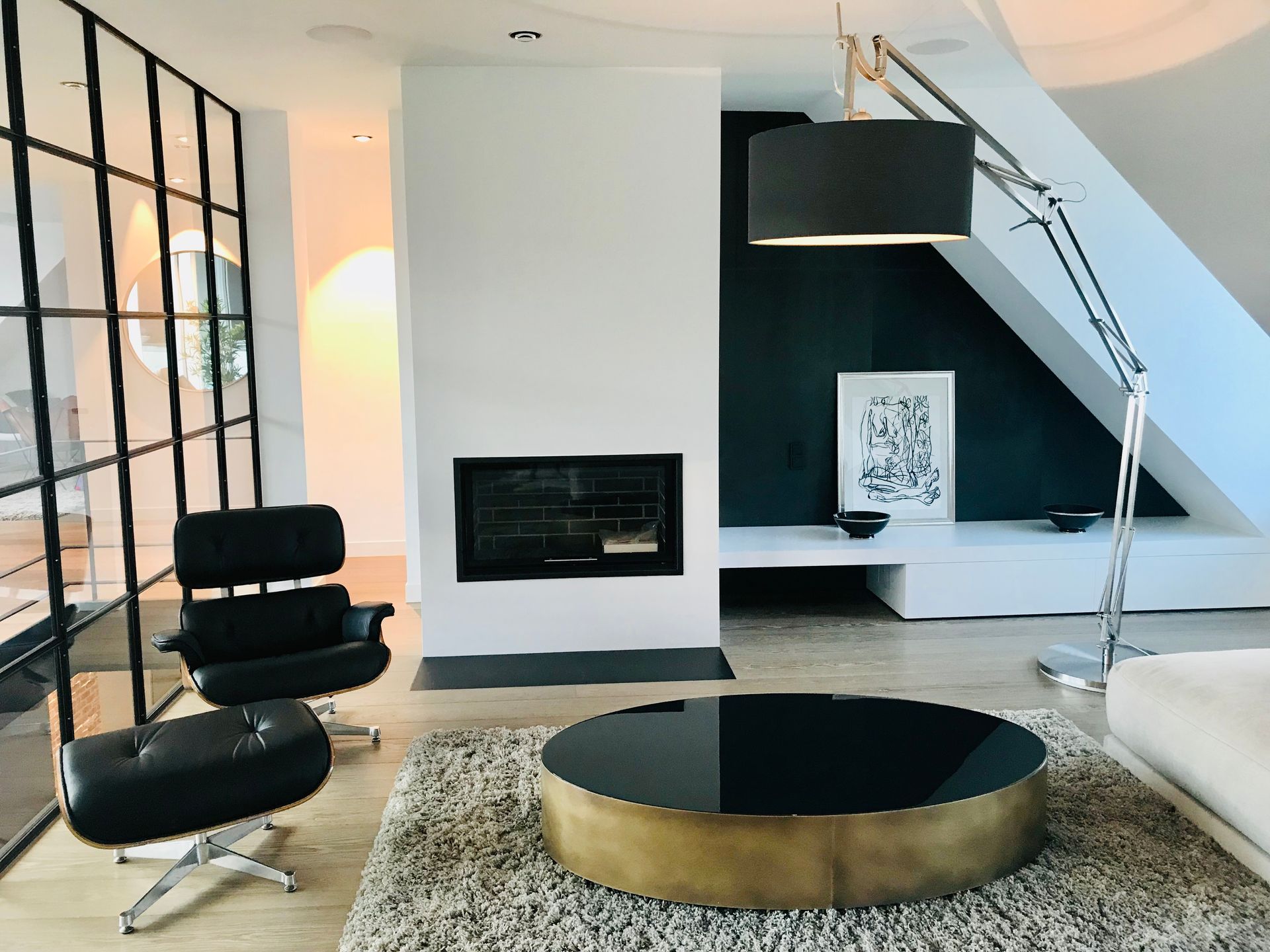 Modern living room with black fireplace, lounge chair, round coffee table, and staircase