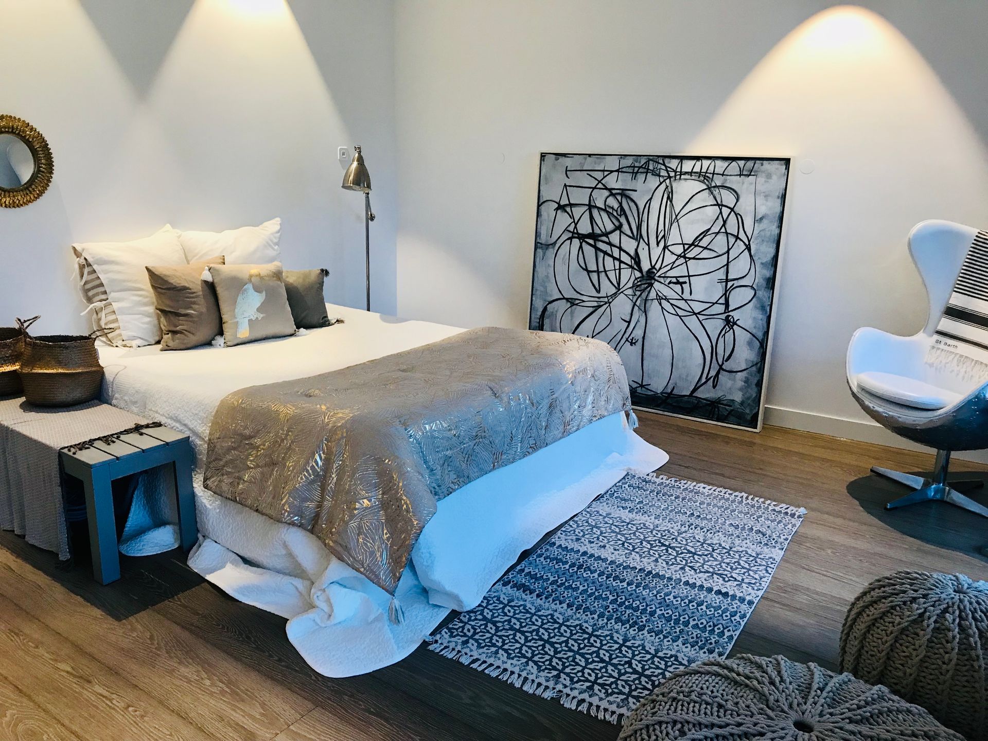 Modern bedroom with a bed, patterned rug, artwork, and a white accent chair under wall sconces