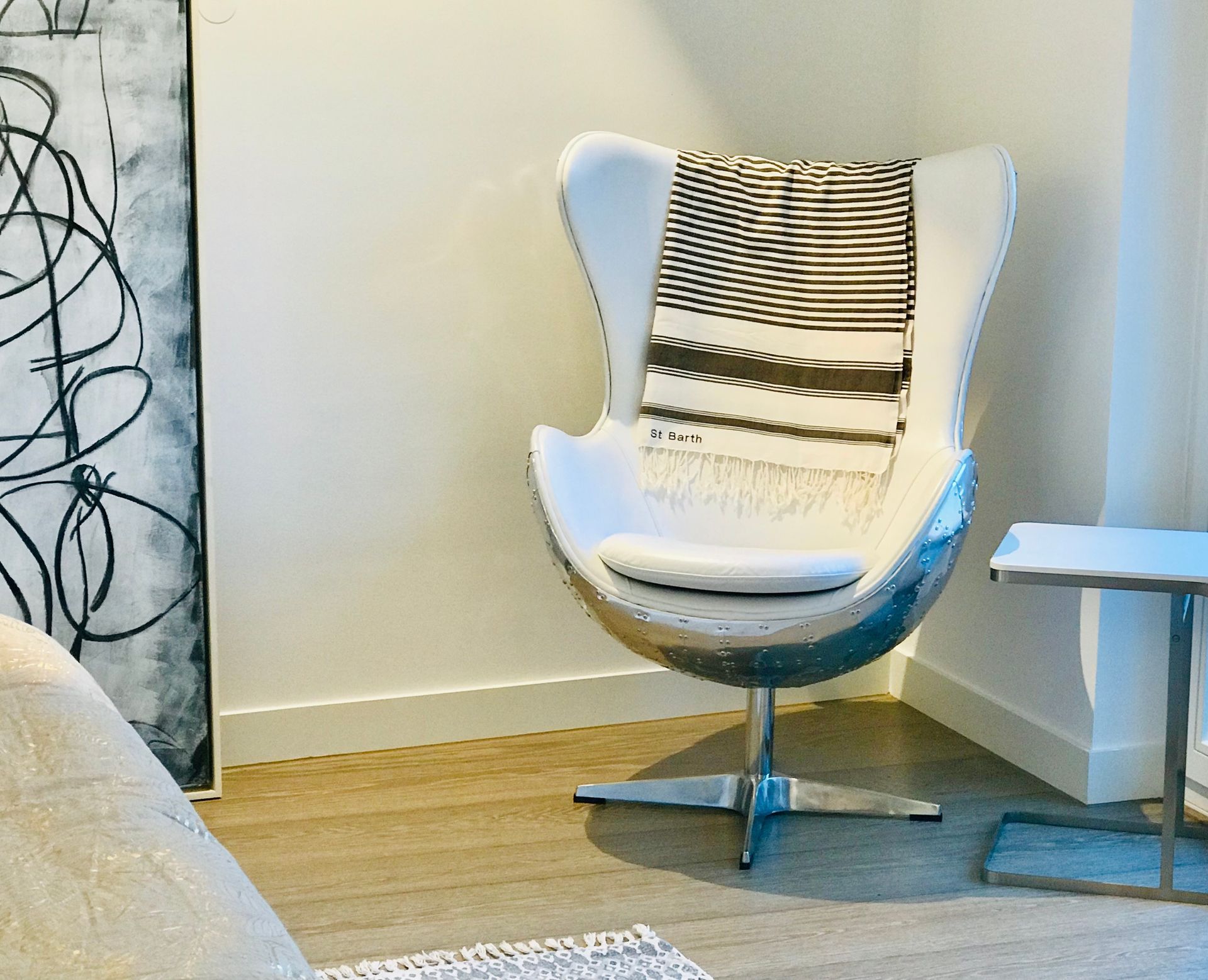 White modern chair with striped throw blanket in a bright living room corner, beside a small white side table