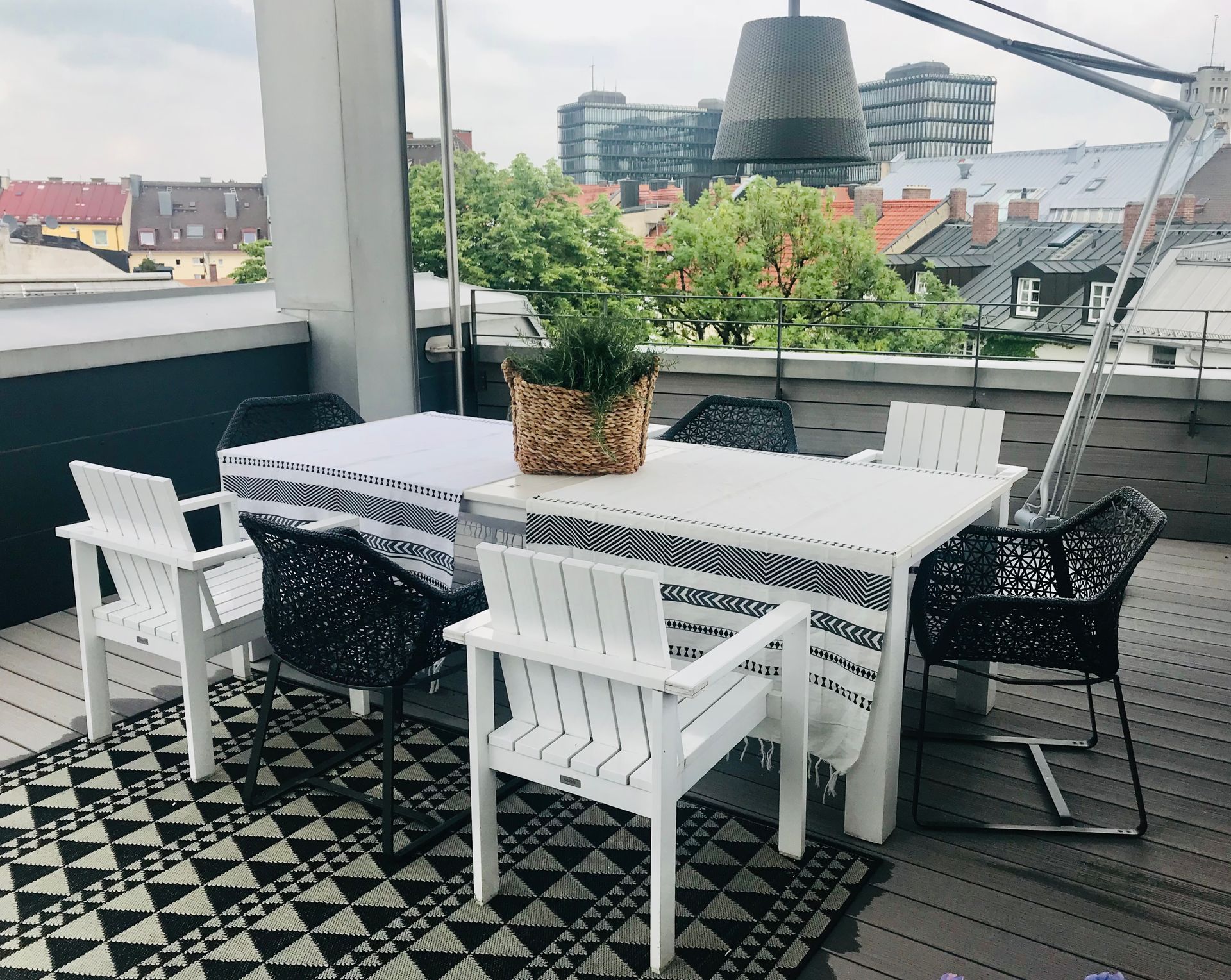 Outdoor patio with white and black chairs, a table, patterned rug, and city buildings in the background