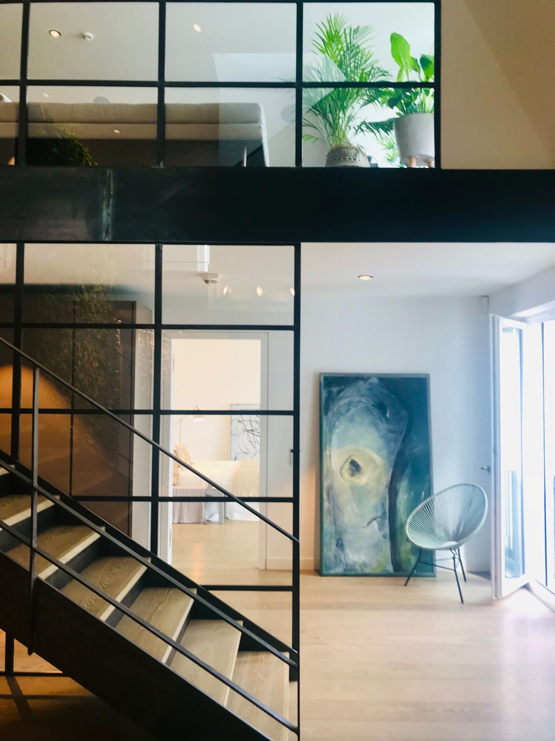 Modern loft interior with black staircase, glass railing, large abstract art, and bright plants near a window