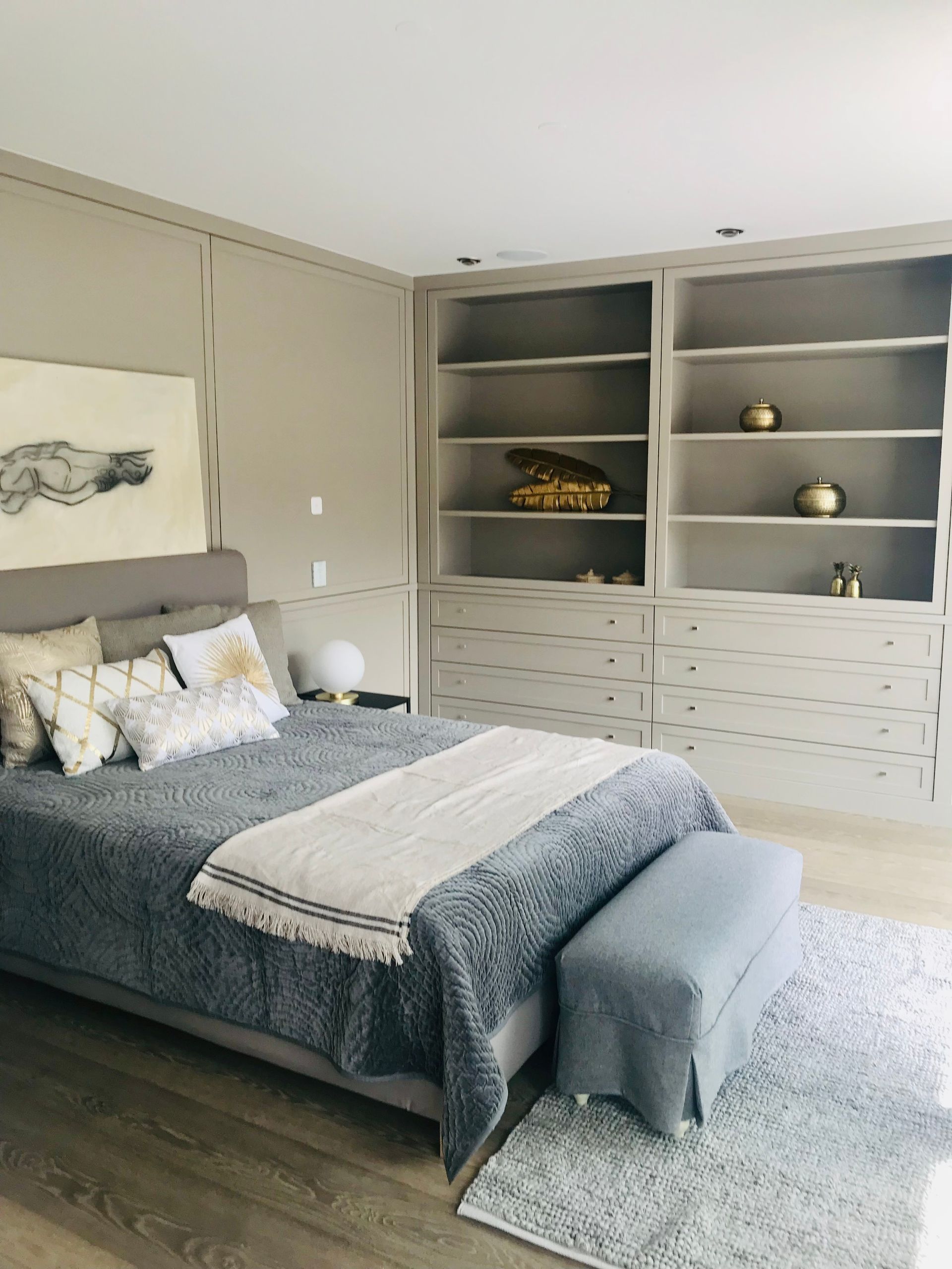 Modern bedroom with gray bed, patterned pillows, built-in shelves, and a tufted bench at the foot of the bed