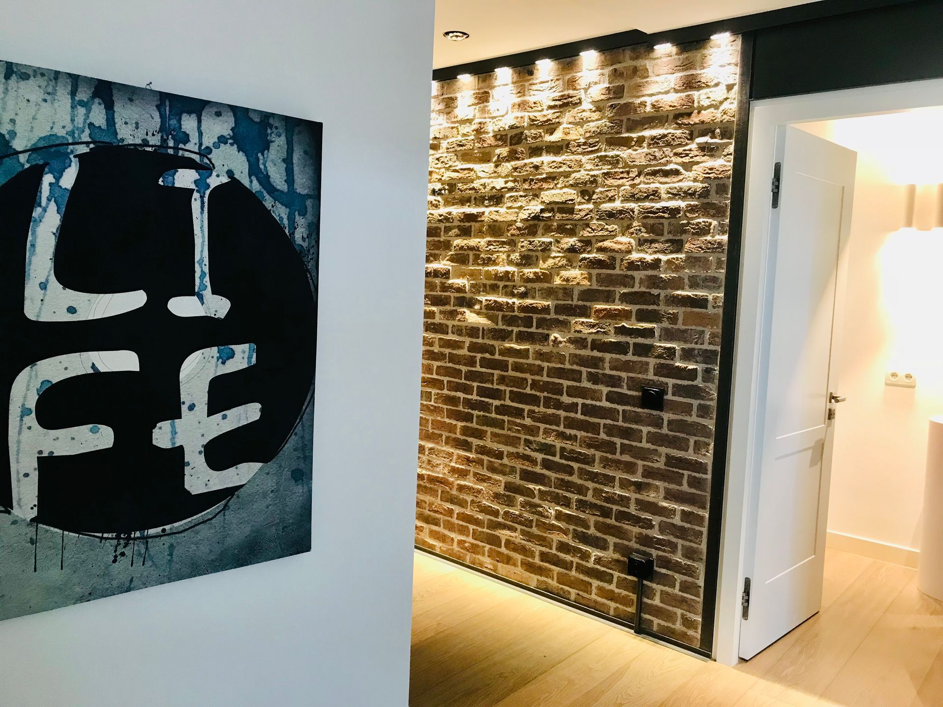 Modern hallway with brick wall, open white door, and black-and-white wall art reading “LIFE”