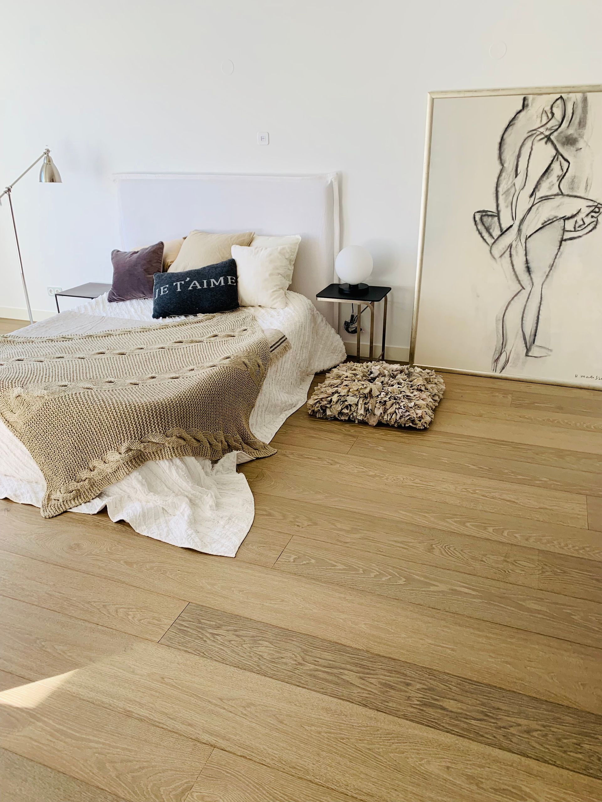 Minimalist bedroom with an unmade bed, cream walls, and abstract line-art leaning against the wall