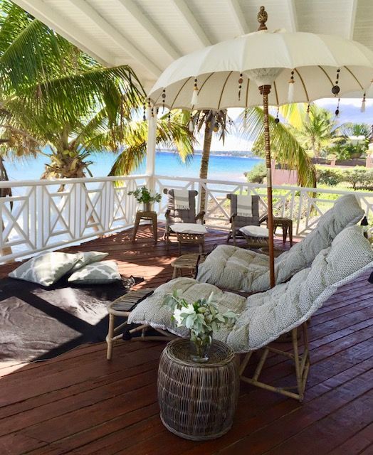 Beachfront deck with cushioned wicker seating, white umbrella, and ocean view through palm trees