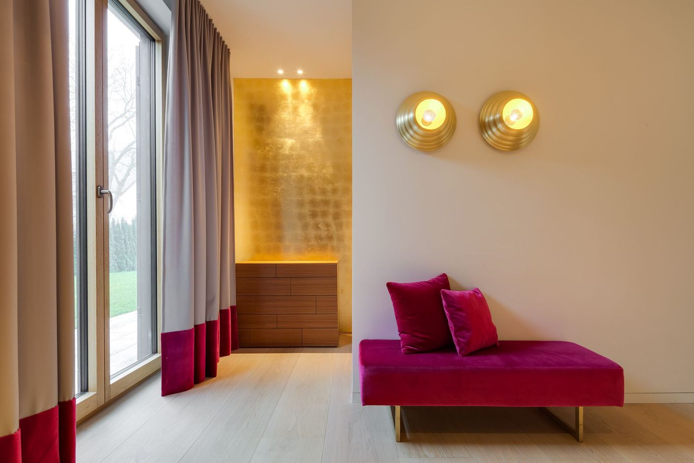 Modern bedroom with pink chaise, wall sconces, large window, and warm wood accents