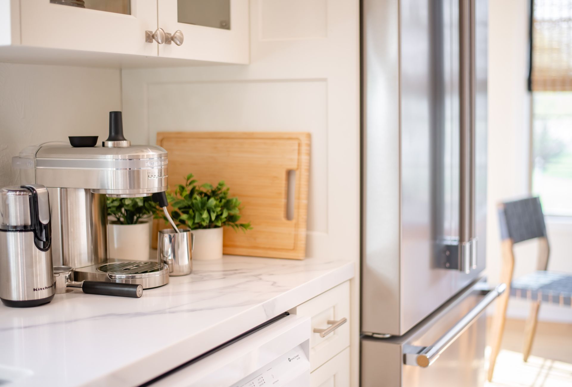 Bright kitchen counter with stainless coffee maker, potted plant, and a silver refrigerator