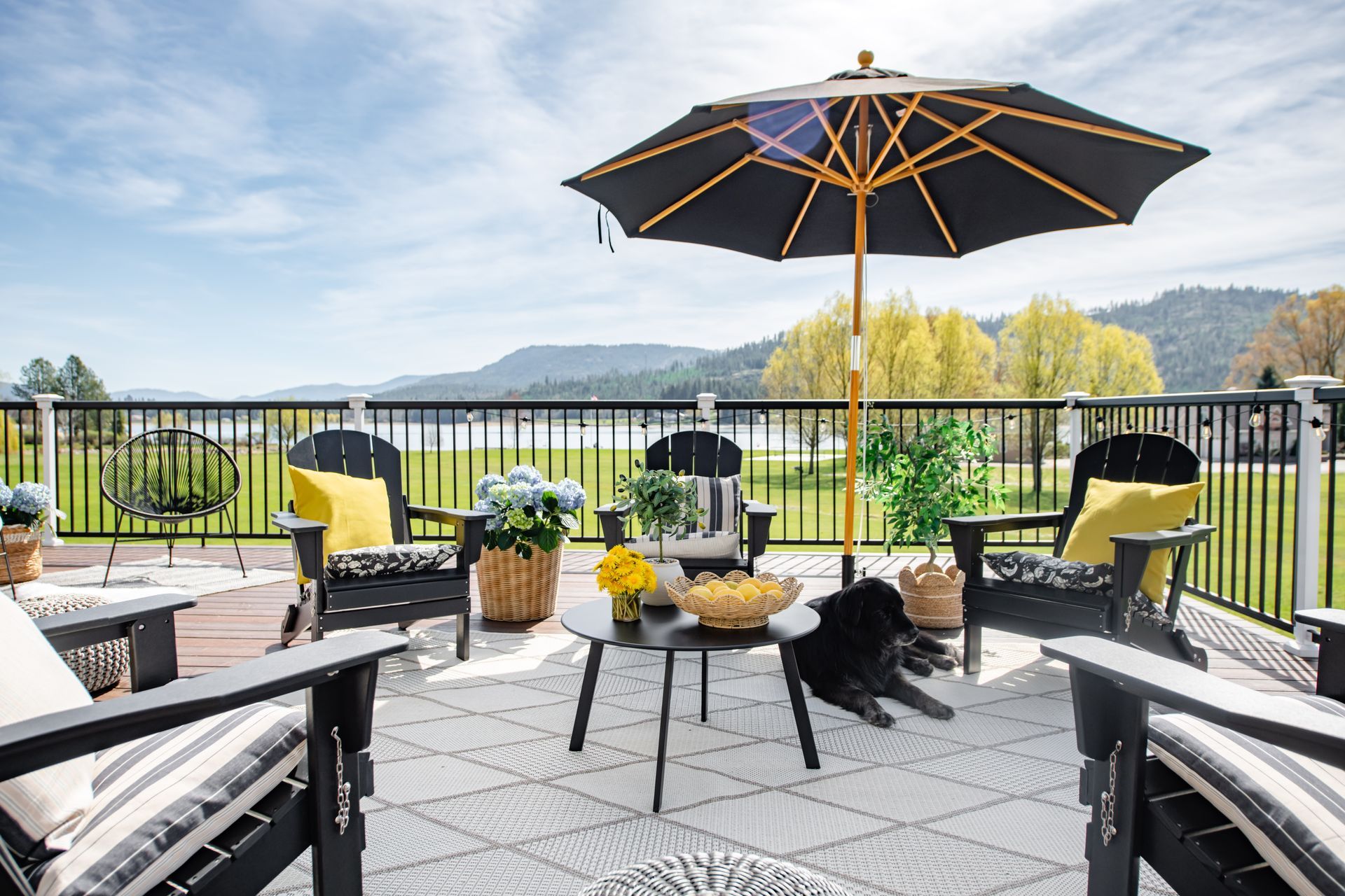 Patio deck with black chairs, table, umbrellas, and potted flowers overlooking a green landscape