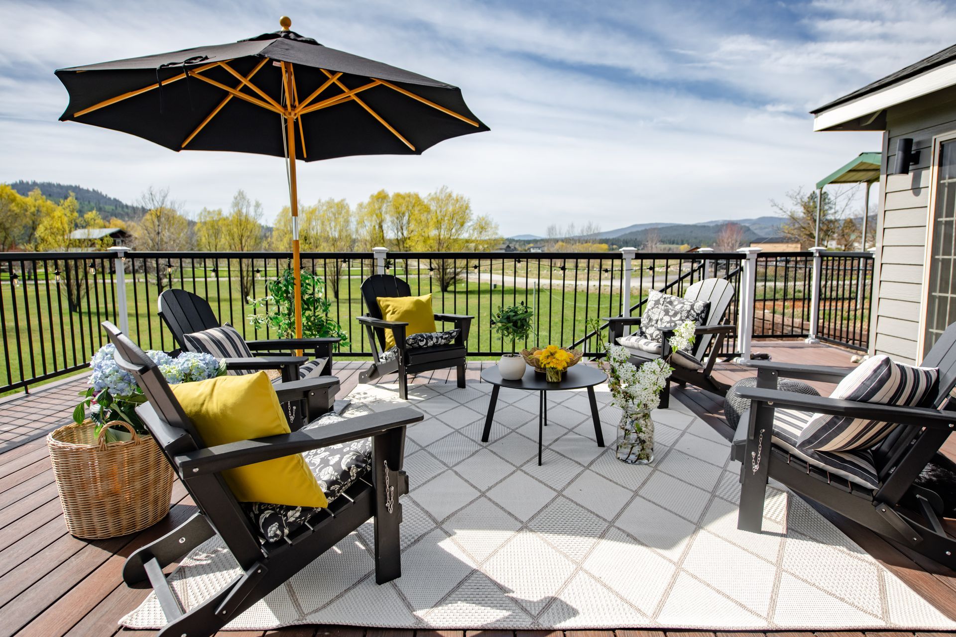 Patio with black chairs, yellow cushions, umbrella, and distant hillside view under a blue sky