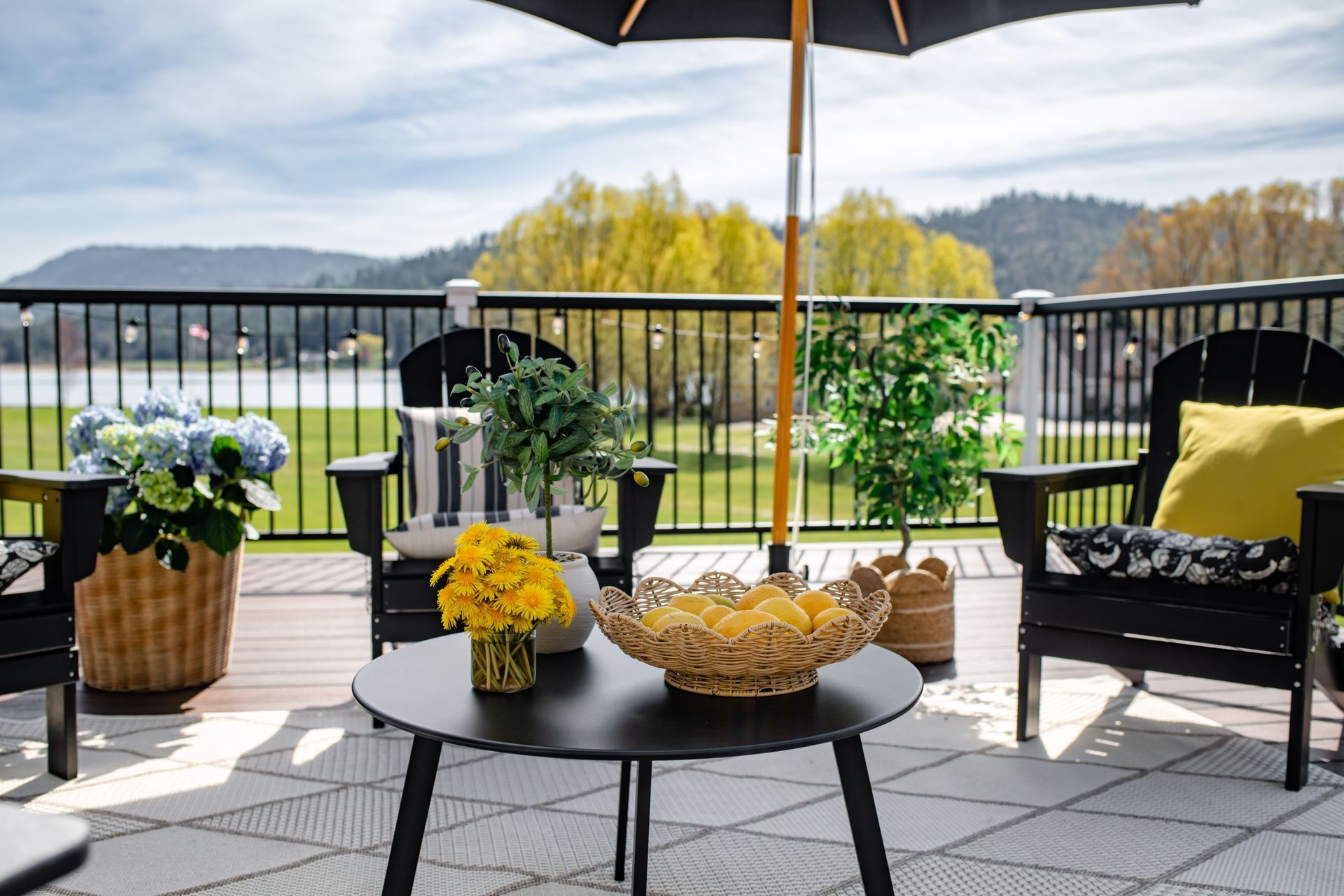 Patio seating with potted flowers, a fruit bowl, and lake view under an umbrella