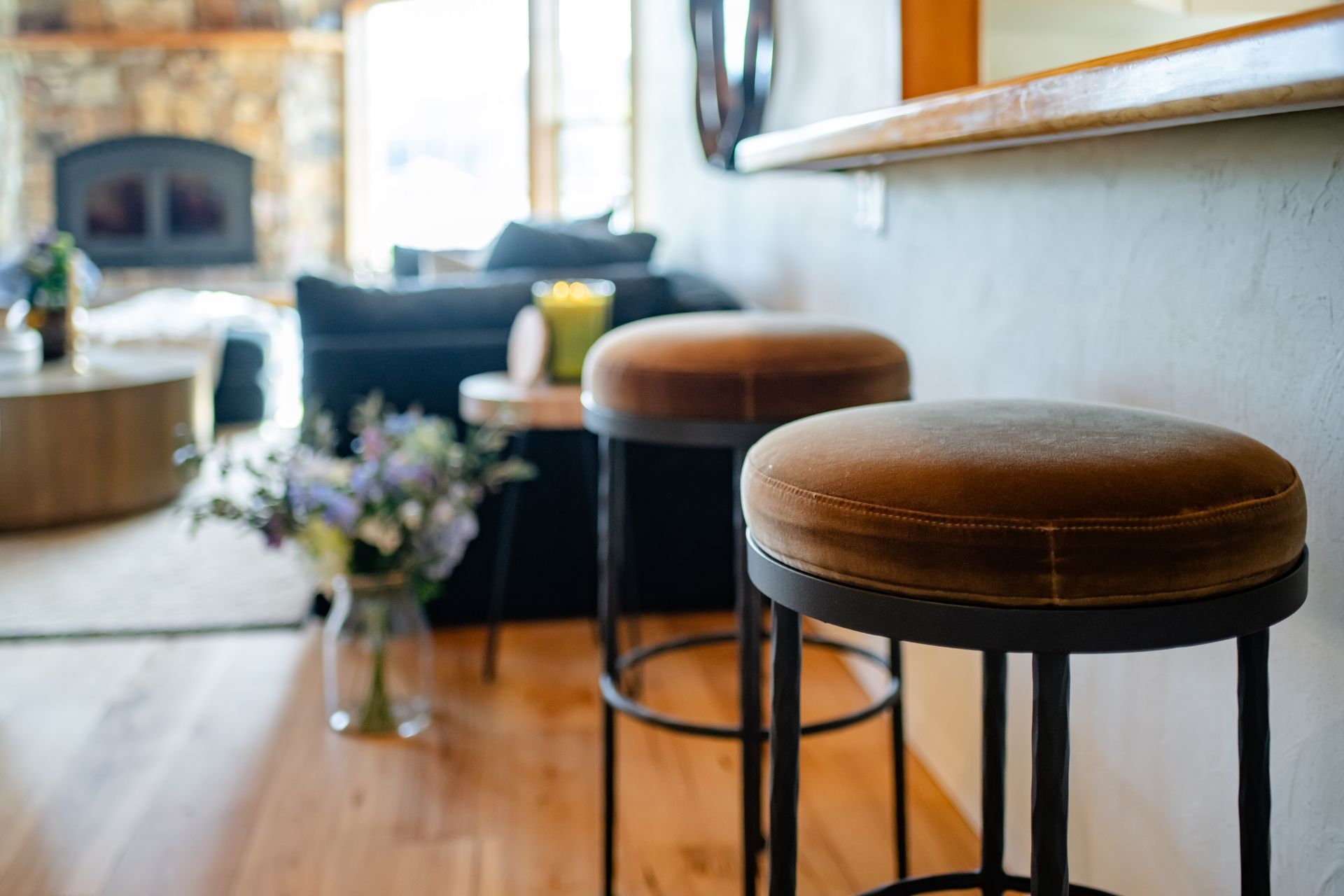 Cozy living room with brown bar stools, wooden floor, blue sofa, and a vase of flowers.