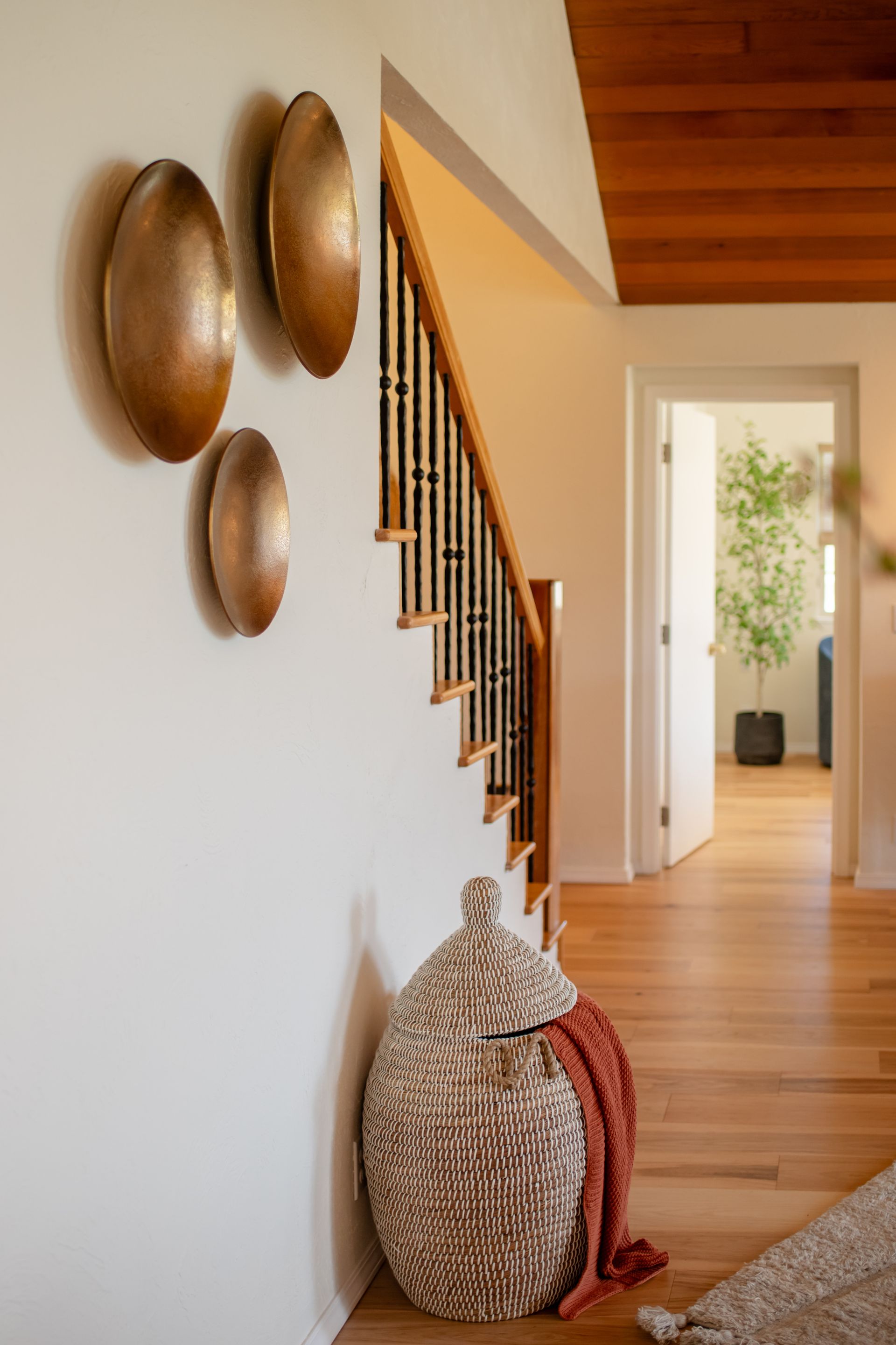 Modern hallway with wood floors, staircase, woven baskets, and decorative wall bowls