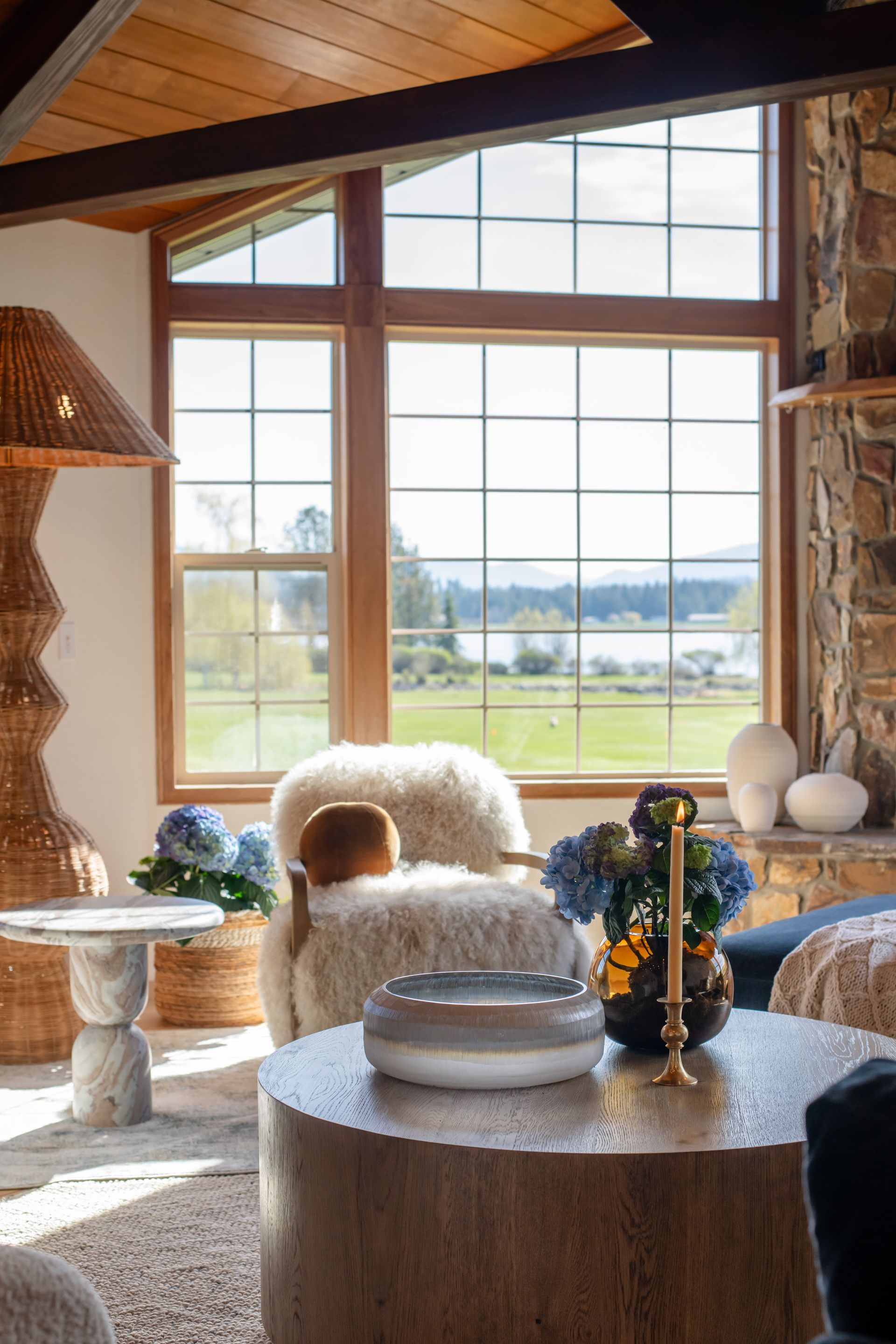 Cozy living room with vaulted wood ceiling, stone fireplace, large windows, and blue sofas