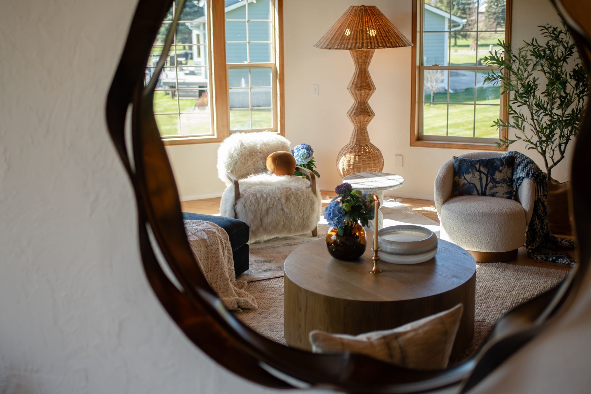 Cozy living room with round coffee table, wicker lamp, and armchairs by bright windows