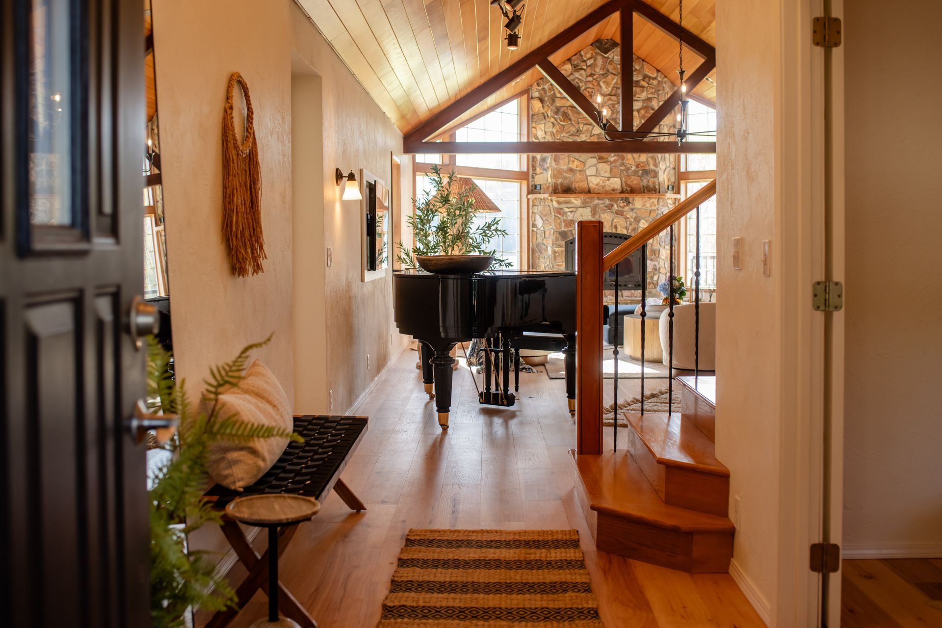Bright hallway with wood floors, potted plants, piano, and glass doors leading to a staircase.