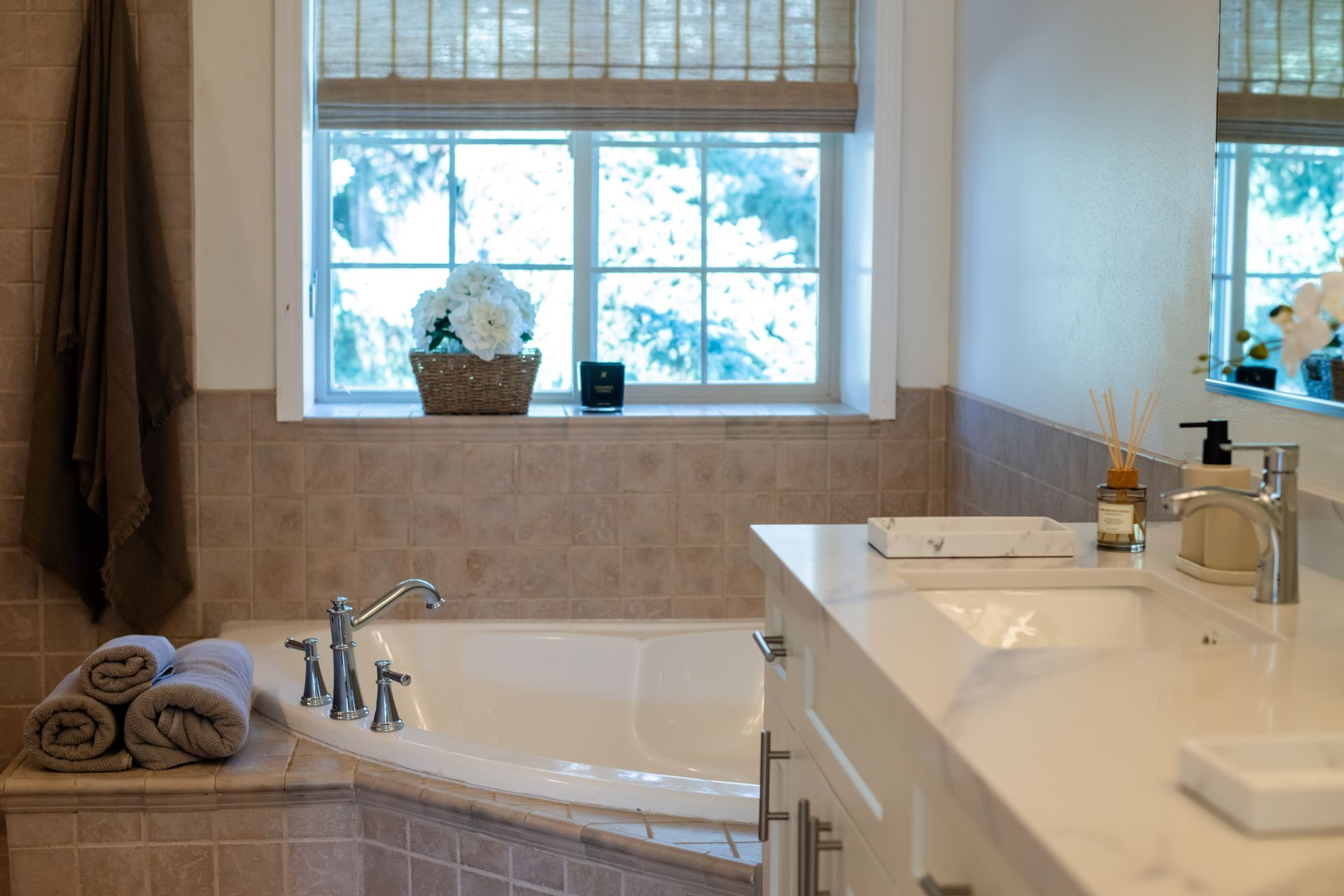 Bright bathroom with a bathtub, white vanity, and window with potted plant above it.