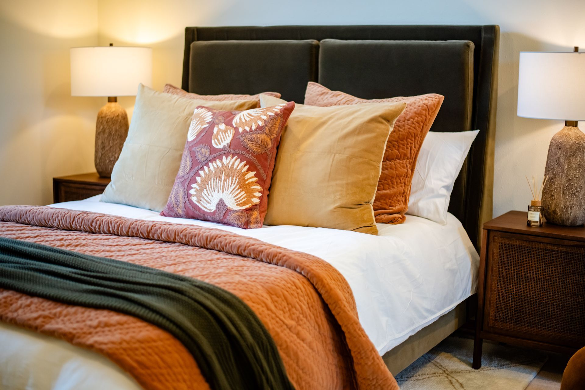 Cozy bed with layered pillows, orange throw blanket, and bedside lamps in a warm bedroom
