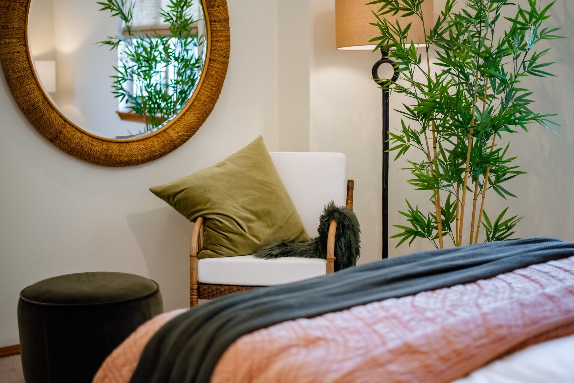 Cozy bedroom corner with round mirror, white chair, olive pillow, black stool, and potted plant