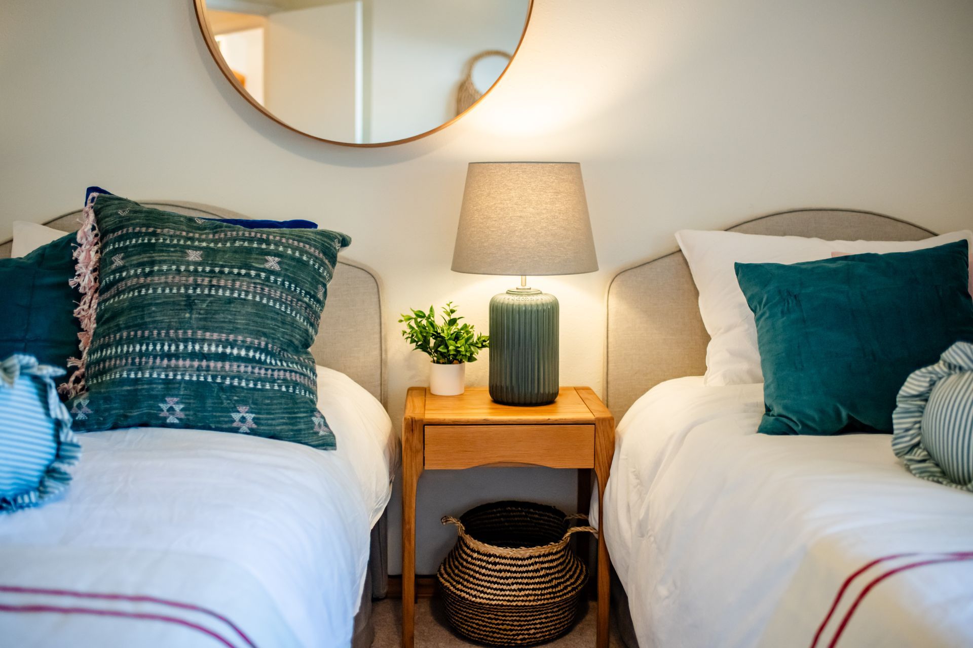 Two neatly made twin beds with teal pillows, a lamp, and a mirror in a cozy bedroom.