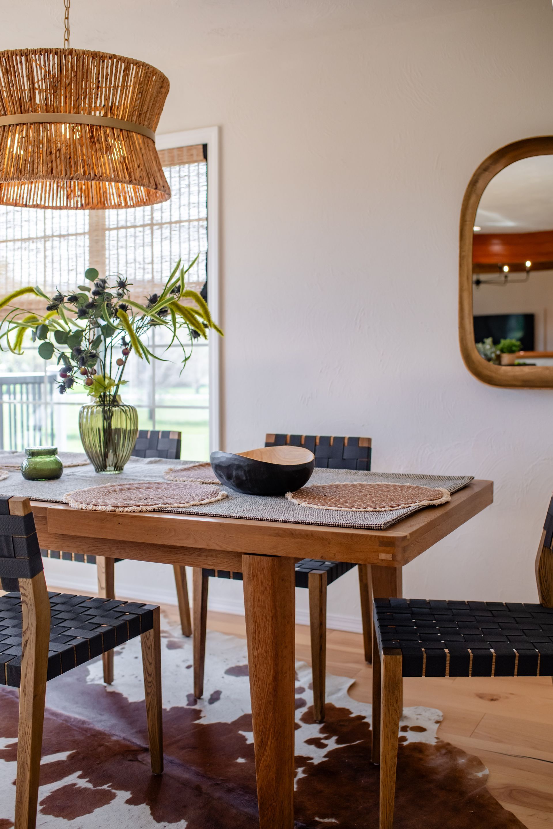 Rustic dining room with wooden table, woven chairs, and vase of flowers by a window