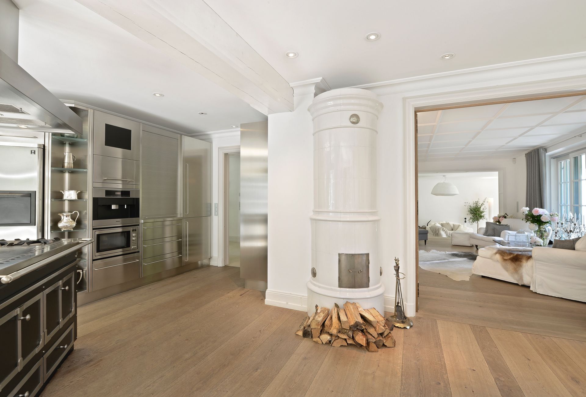 Bright modern living room with white fireplace, wood floors, and adjacent kitchen area.