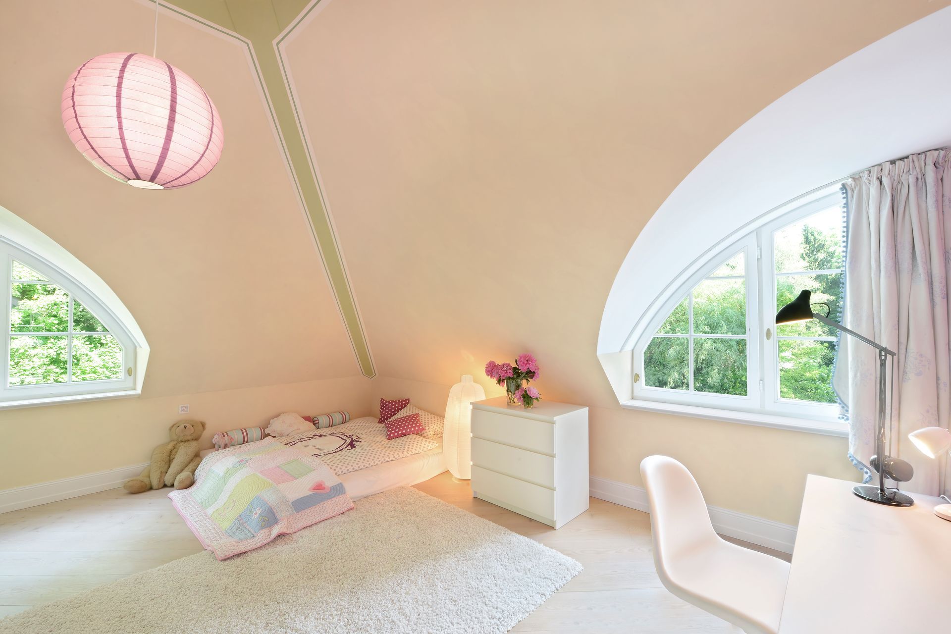 Bright attic bedroom with pink accents, twin windows, a bed, and a white desk chair.