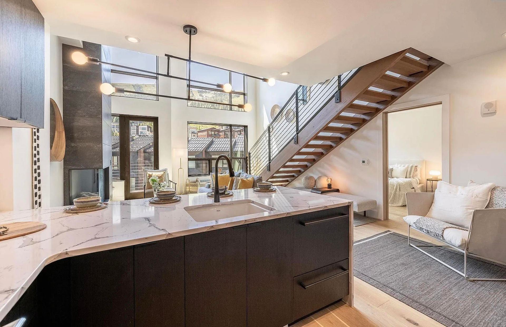 Modern open-plan living room with kitchen island, staircase, and light-colored sofa