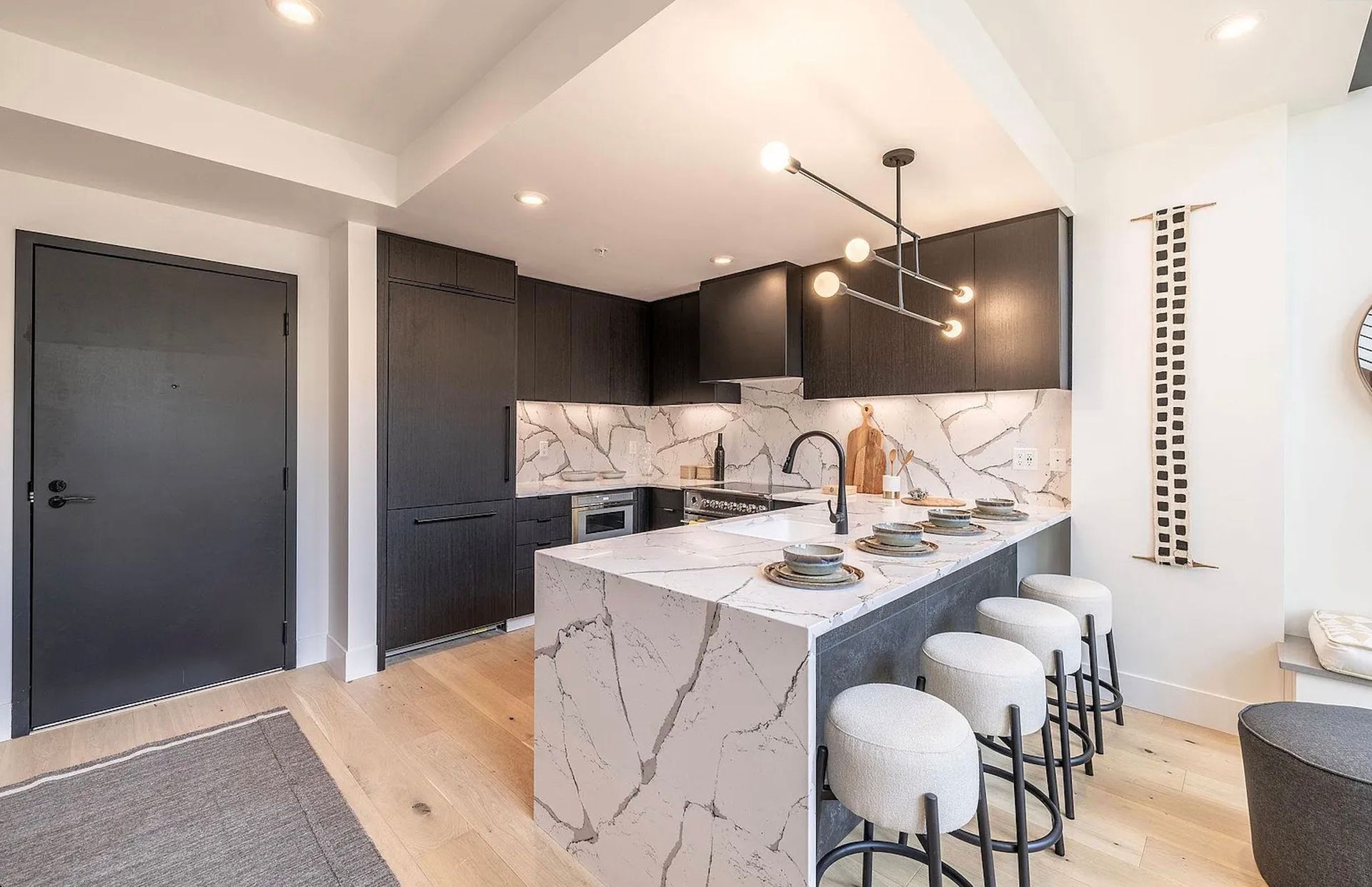 Modern kitchen with dark cabinets, white marble island, pendant lights, and bar stools