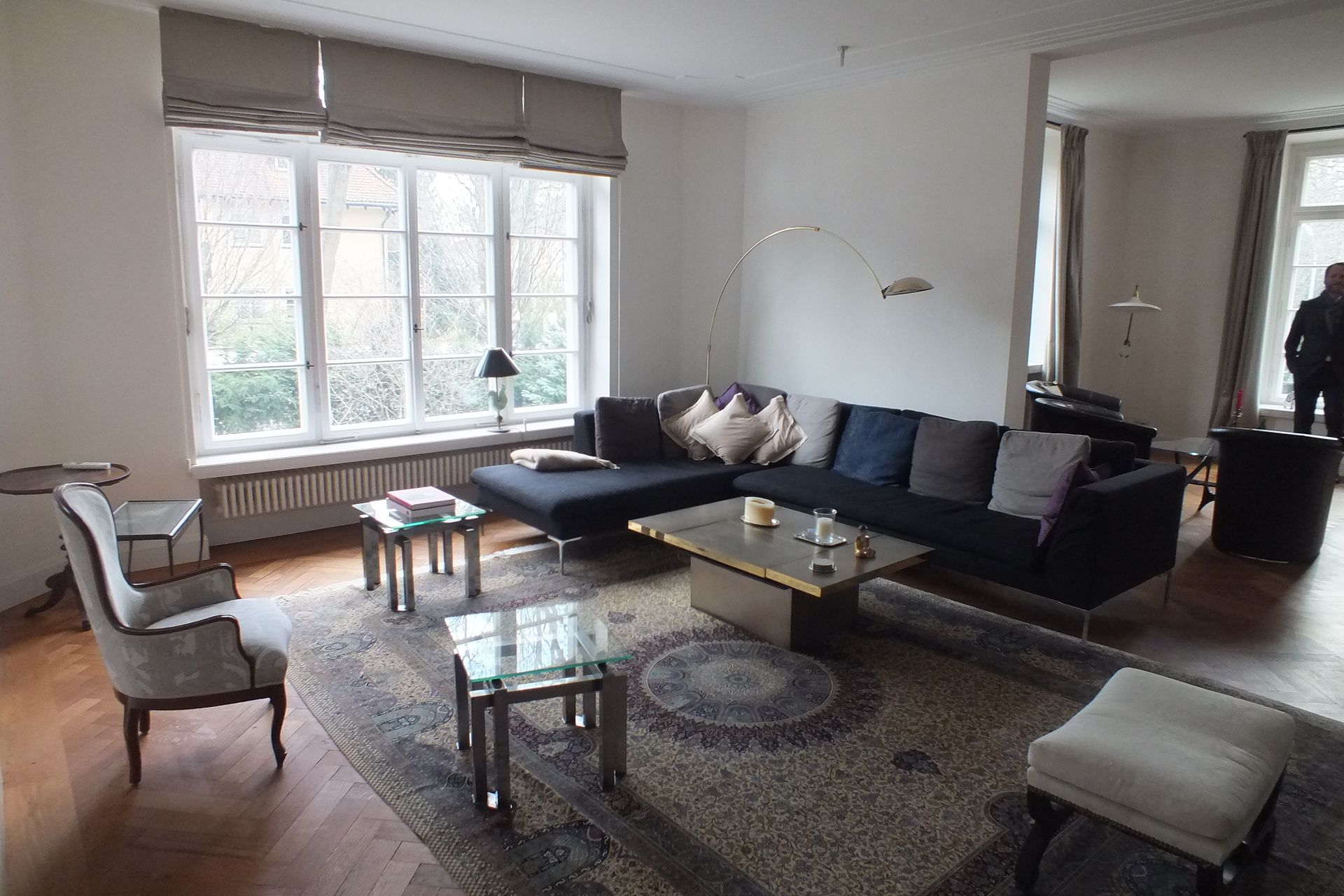 Modern living room with a gray sectional, patterned rug, coffee table, armchair, and large window.
