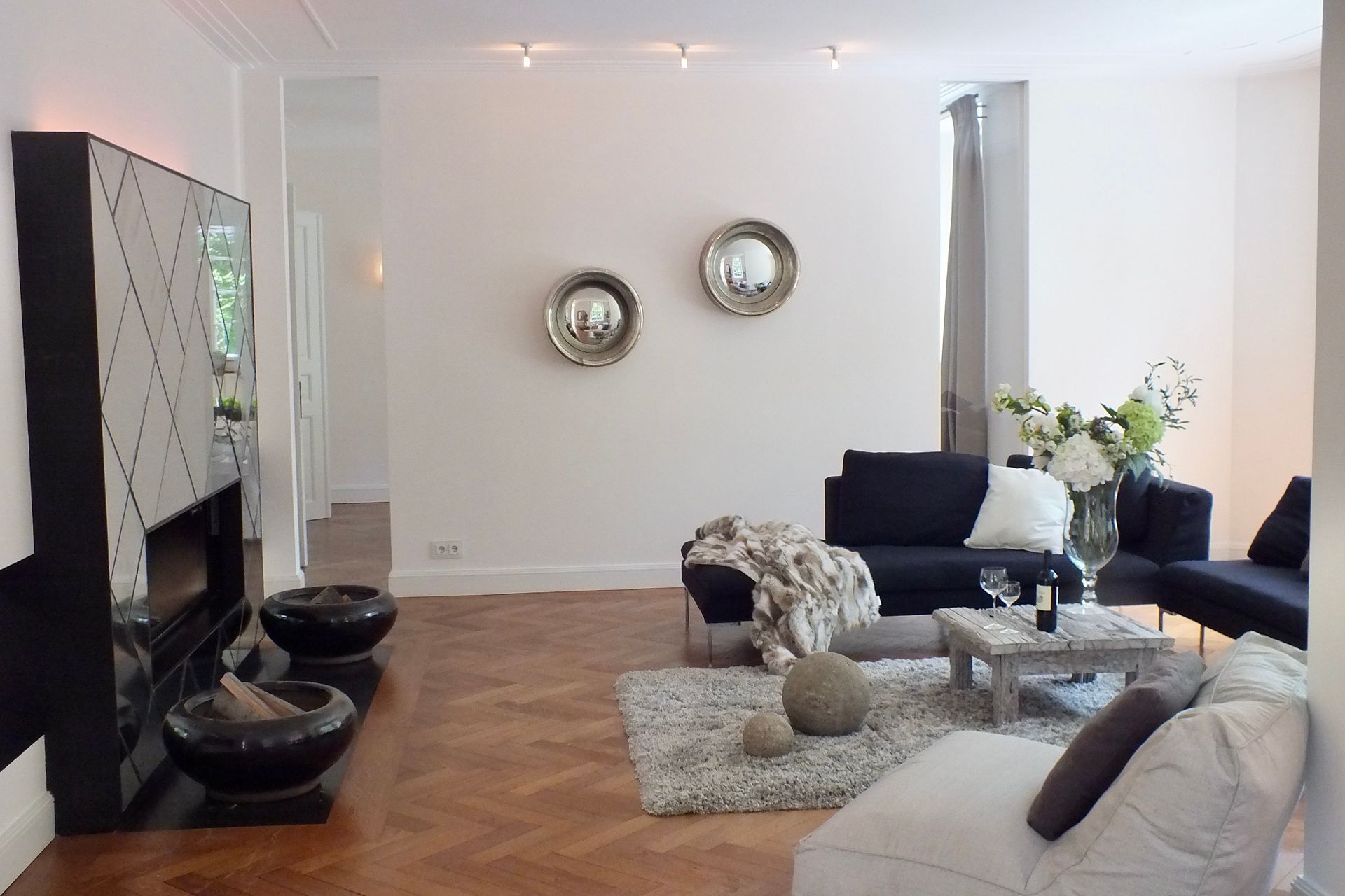 Modern living room with black-and-white furniture, glass coffee table, wall mirrors, and hardwood floor