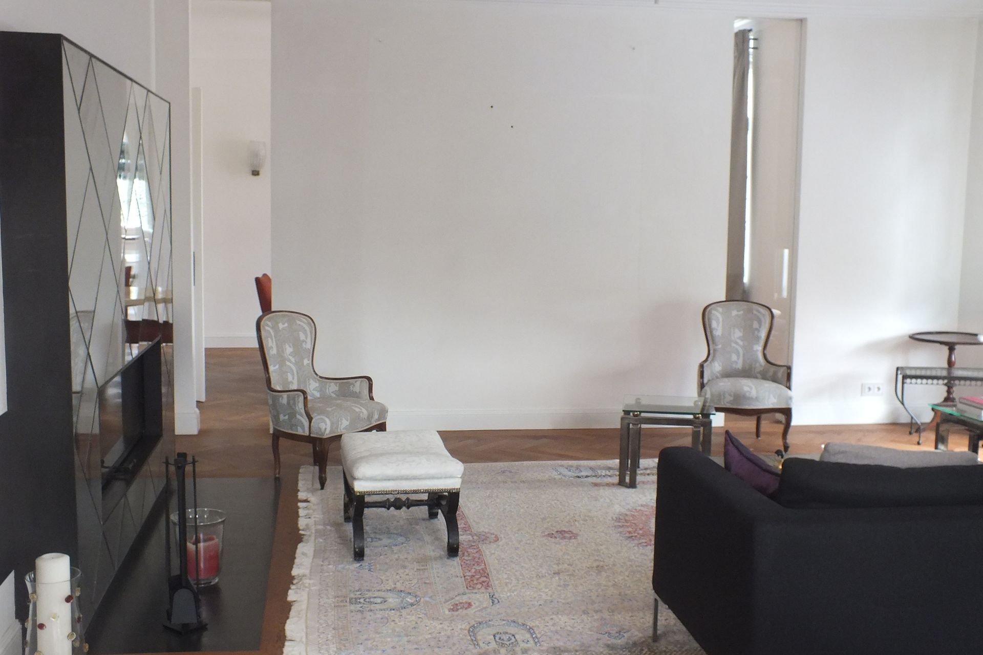 Bright living room with white walls, patterned rug, black sofa, and ornate chairs around a coffee table.