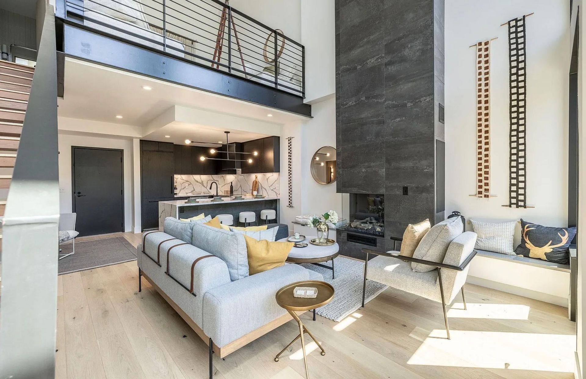 Modern open-concept living room with light sofas, a tall fireplace, and an upstairs balcony.