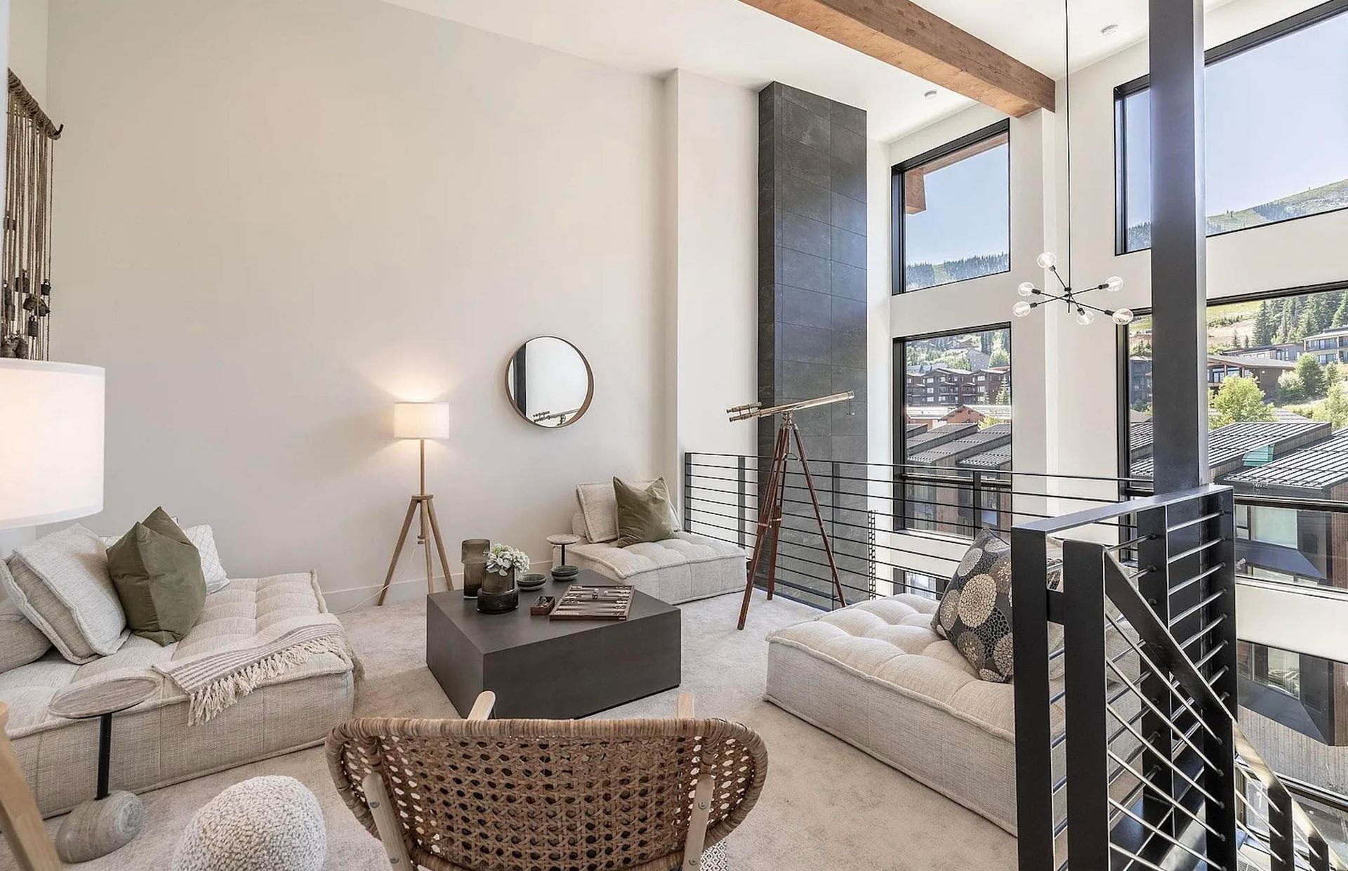 Bright living room with white sofas, a round mirror, and a balcony view through open glass doors