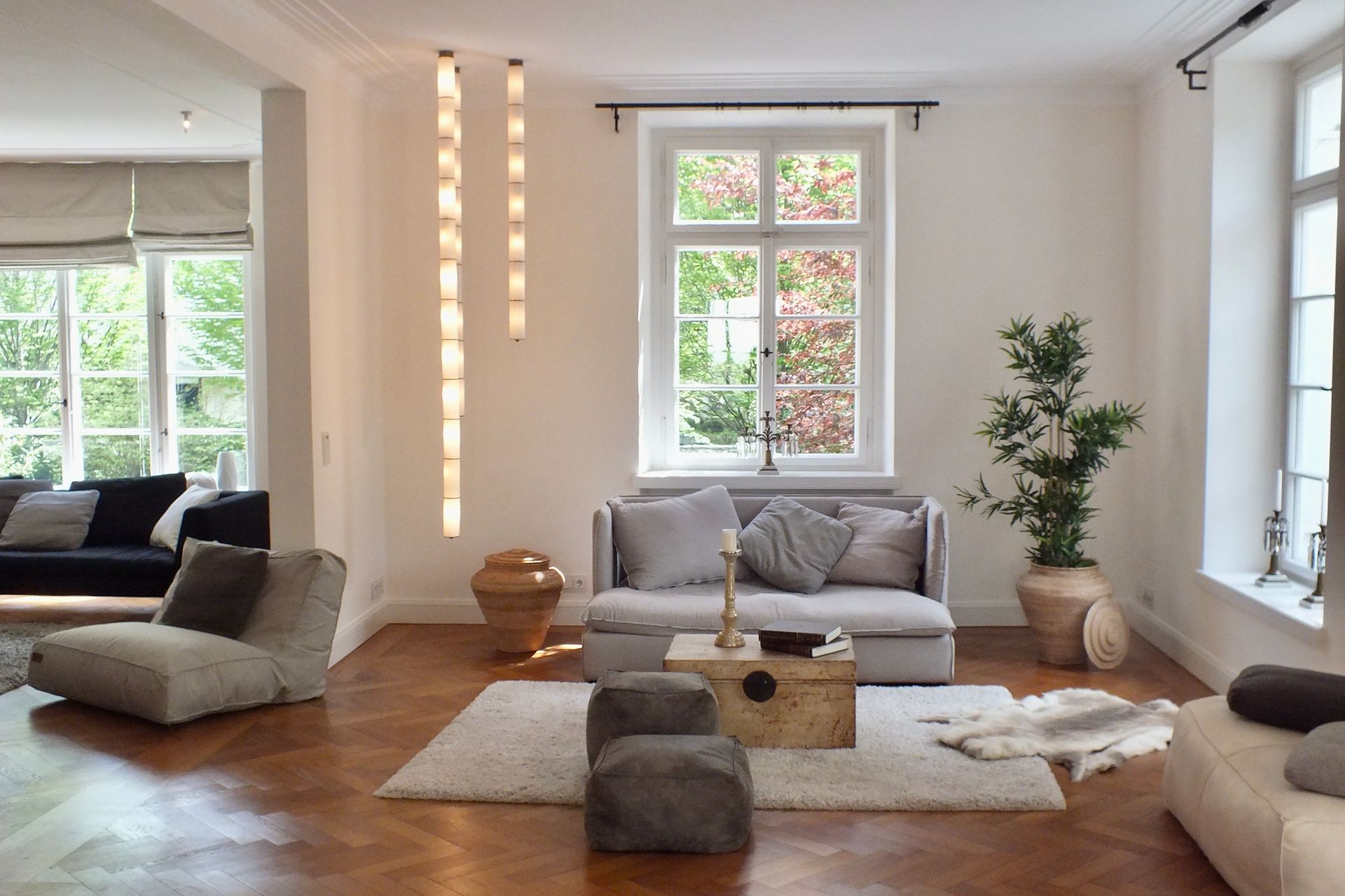 Bright, airy living room with white walls, wood floor, low sofa, rug, and large windows with plants.
