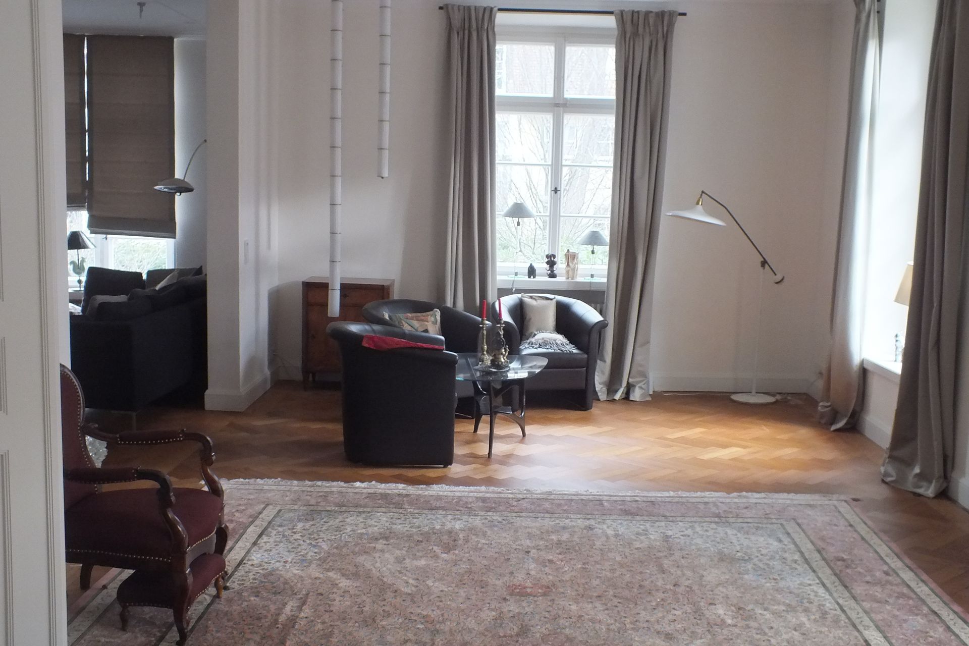 Bright living room with large windows, rugs, chairs, and a floor lamp in soft natural light