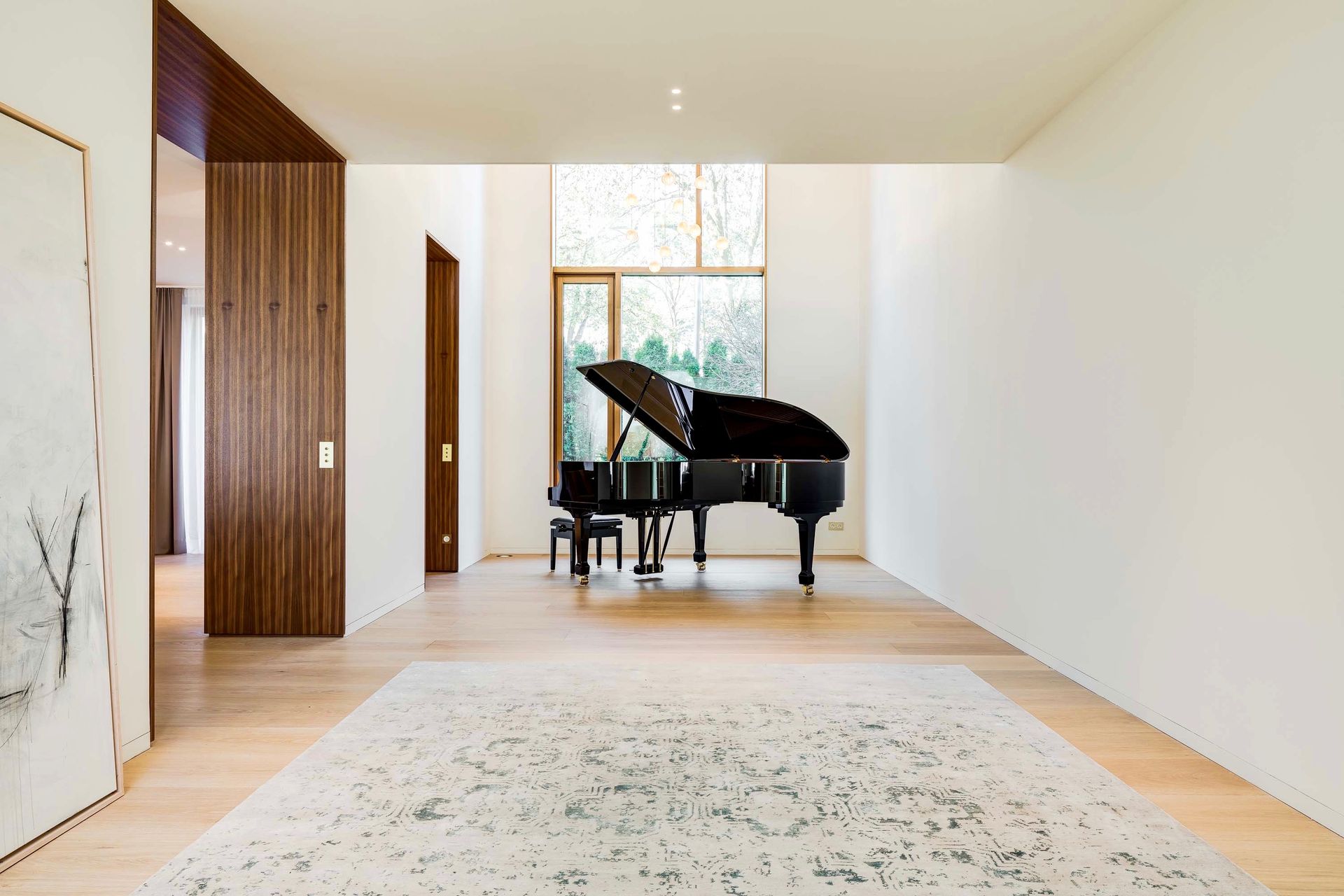 Bright room with a black grand piano, wooden doors, and a patterned rug by a large window