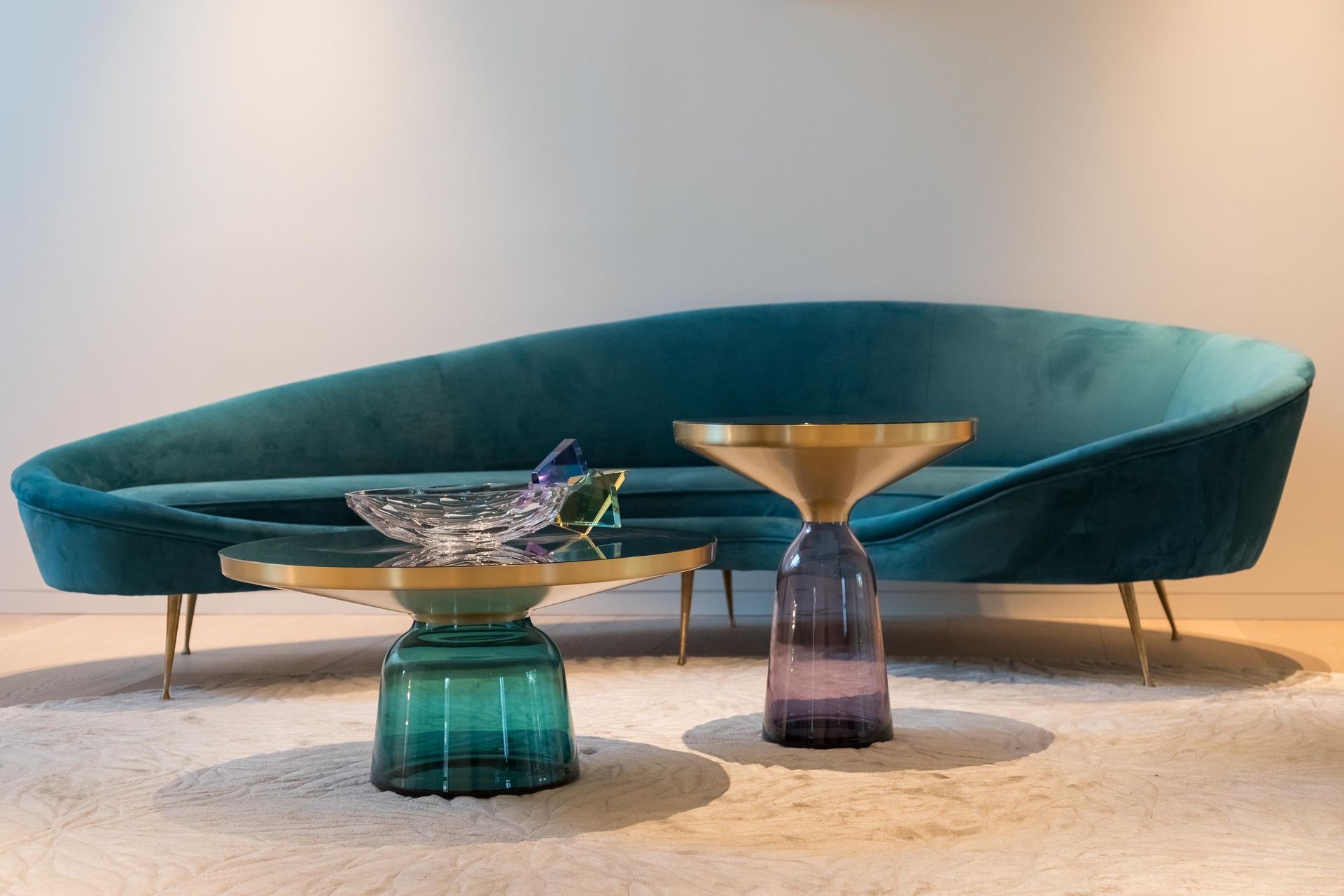 Teal velvet sofa with two glass side tables in a modern living room