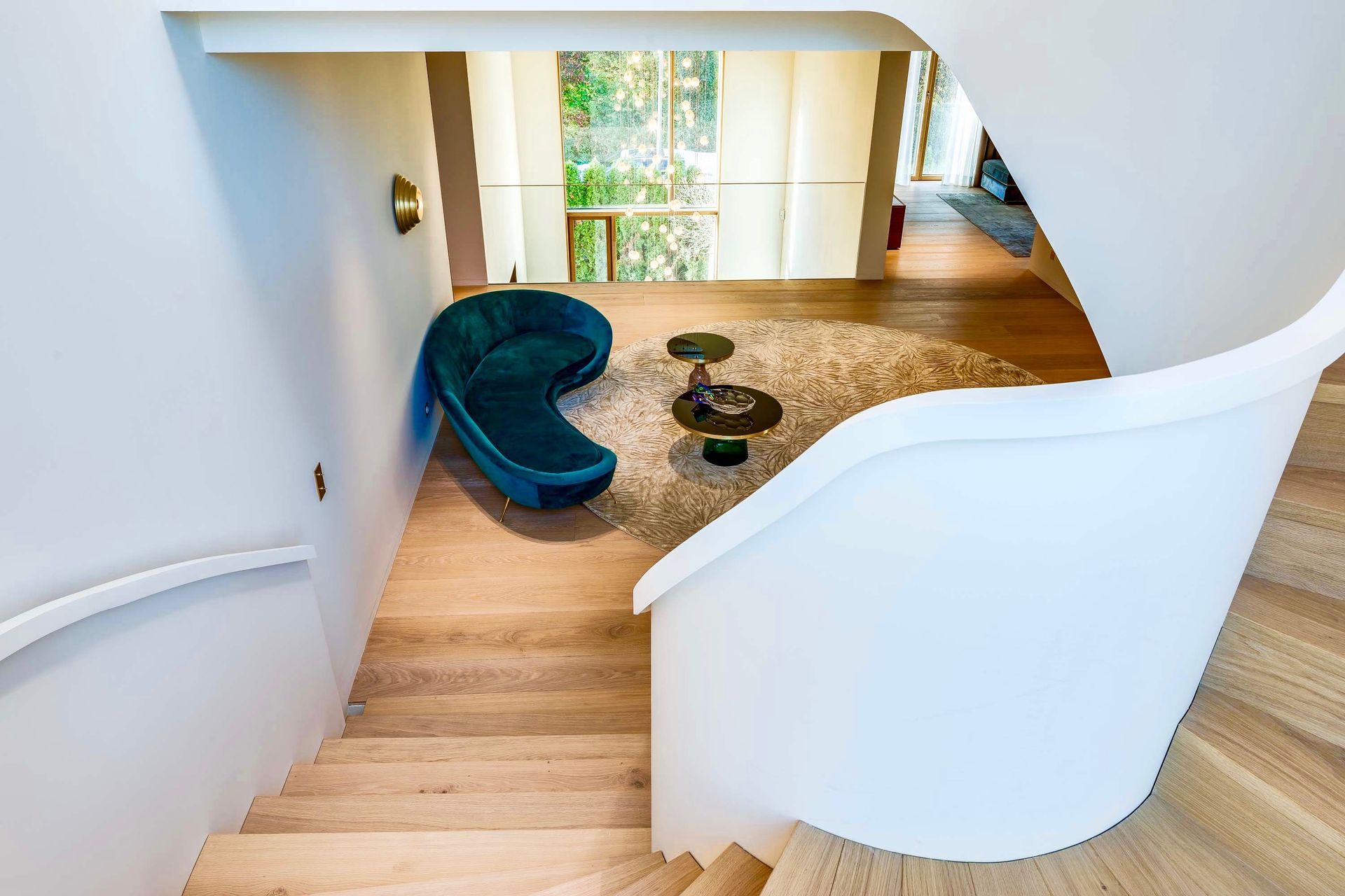 Curved white staircase overlooking a bright living area with teal chair and round coffee table