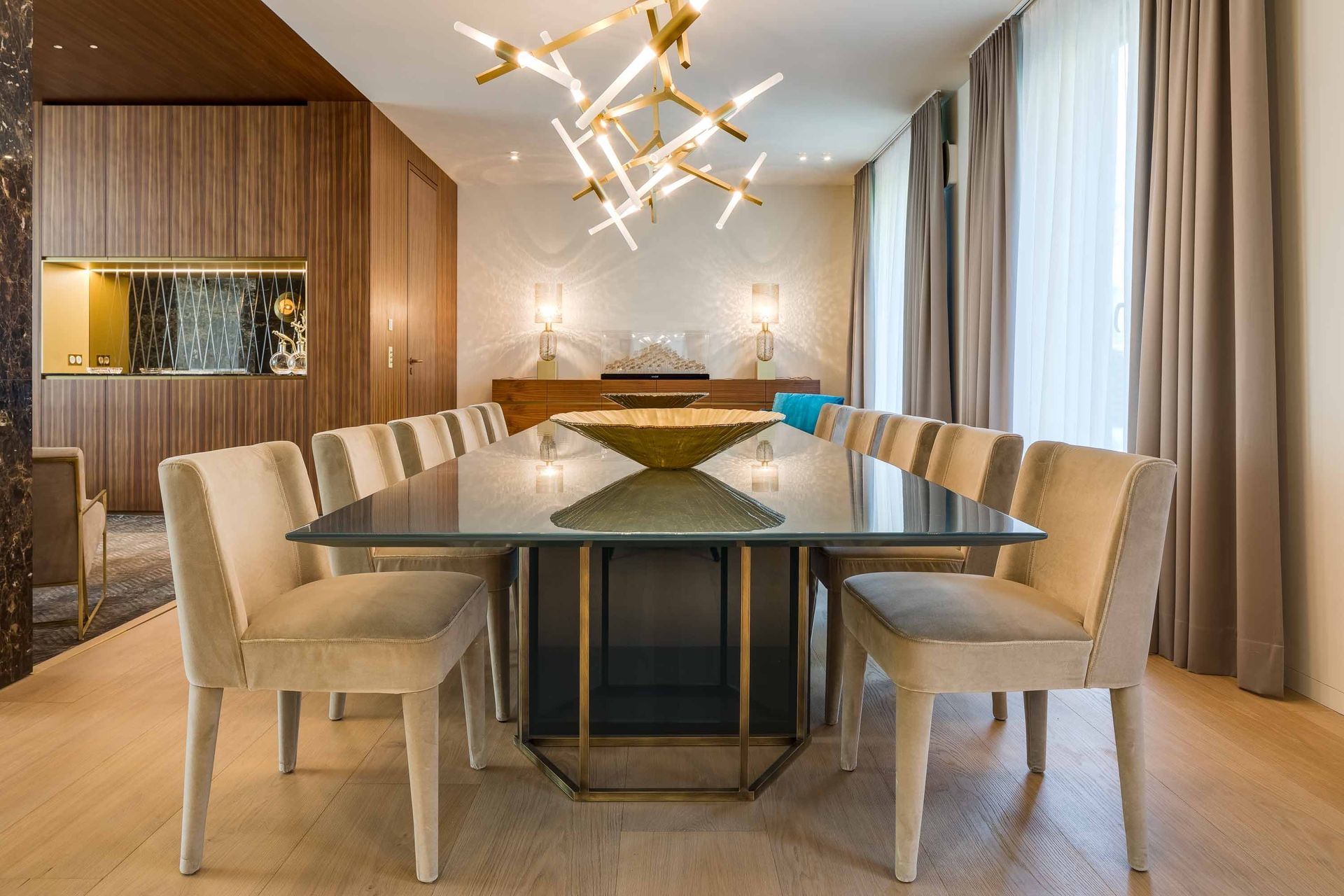 Modern dining room with a glass table, beige chairs, wood-paneled walls, and pendant lighting
