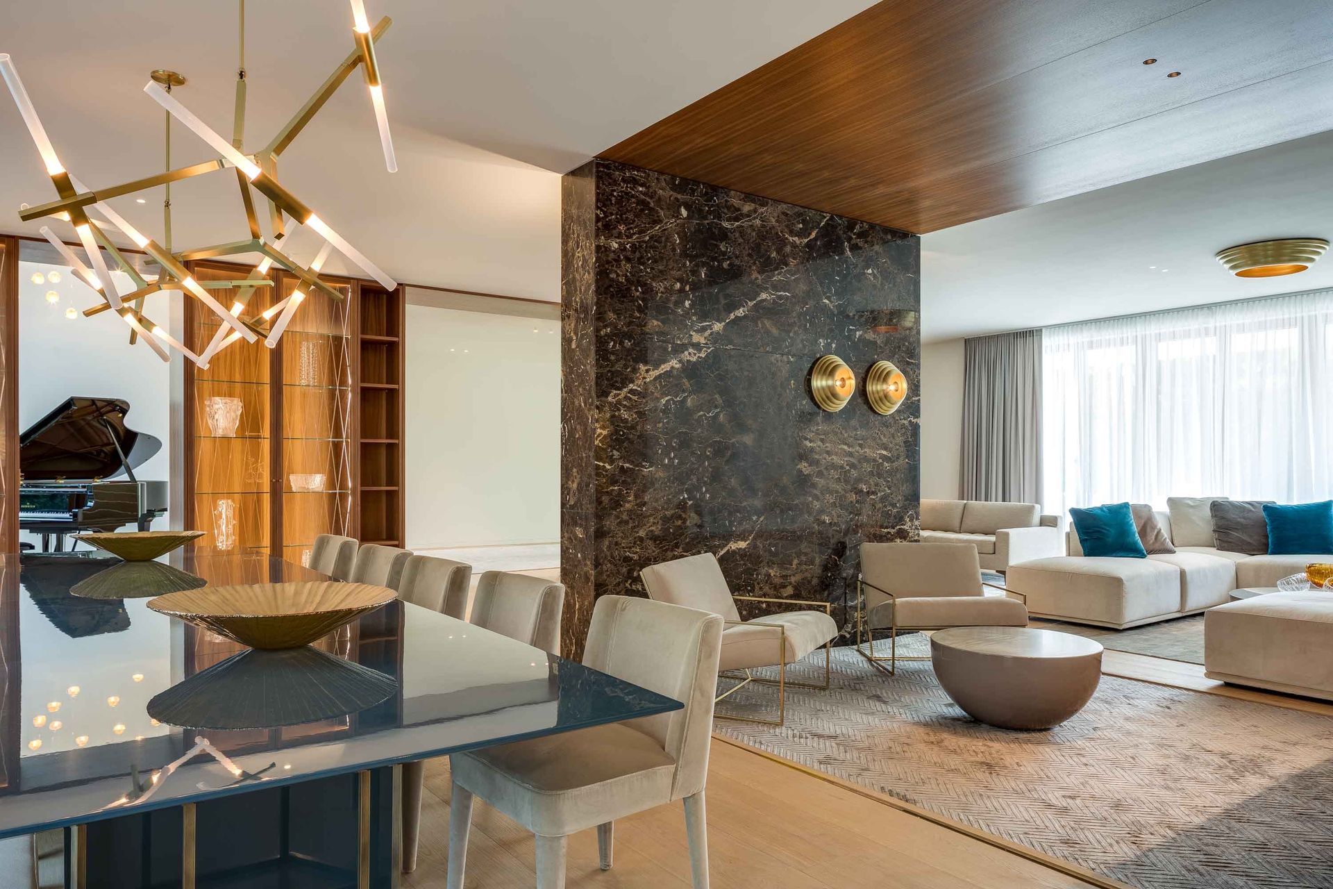 Modern open-plan living and dining room with chandelier, marble table, beige sofa, and dark accent wall