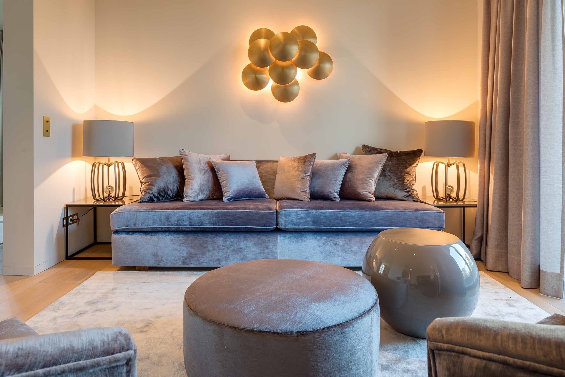 Elegant living room with blue sofa, round ottomans, warm lamps, and wall art.