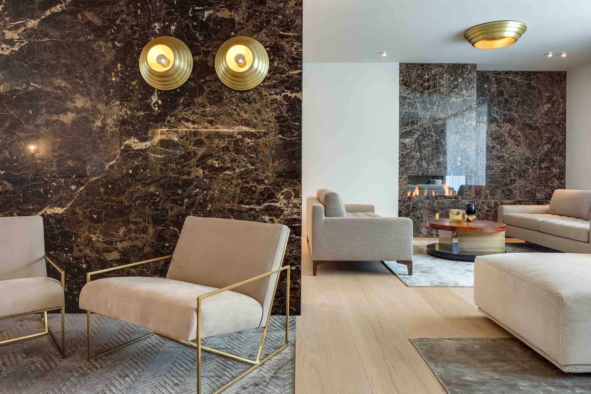 Modern living room with black marble accent wall, gold sconces, beige chairs, and light wood flooring