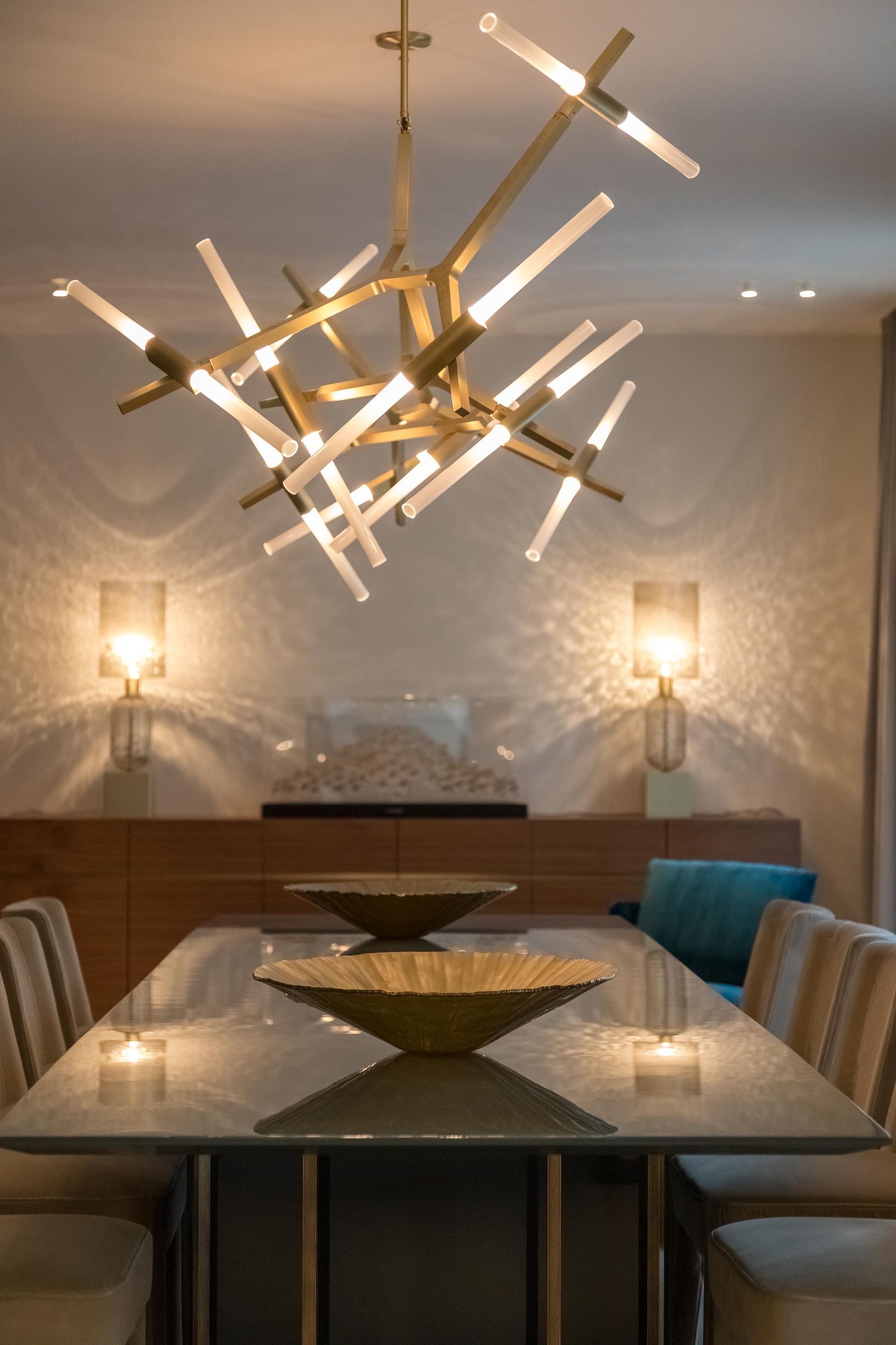 Modern dining room with a long table, upholstered chairs, wall sconces, and a sculptural hanging light fixture