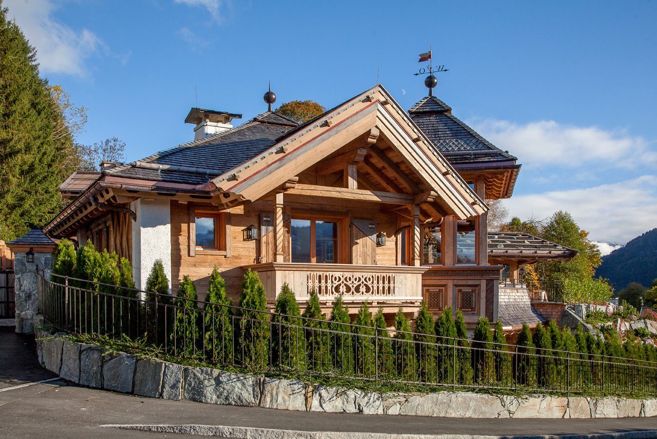 Wooden mountain chalet with stone accents and a fenced garden under a blue sky