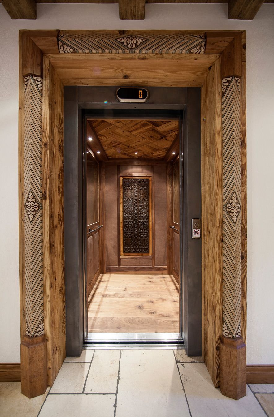 Wood-paneled elevator doorway opening to a warmly lit hallway with decorative walls and stone floor