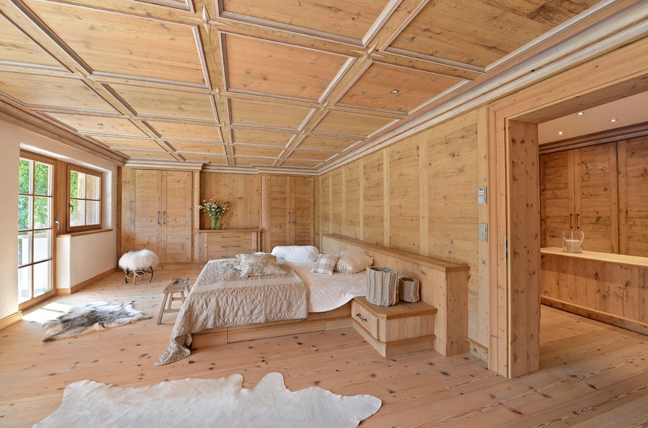 Wood-framed unfinished bedroom with exposed ceiling, windows, and a bed in the center